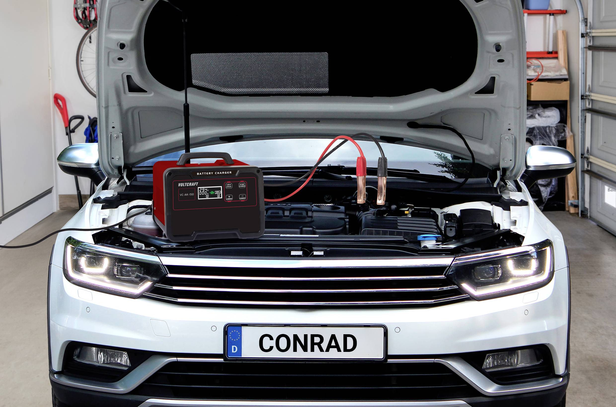 Bílé auto s otevřenou kapotou motoru v garáži. Nabíječka je připojena k baterii.