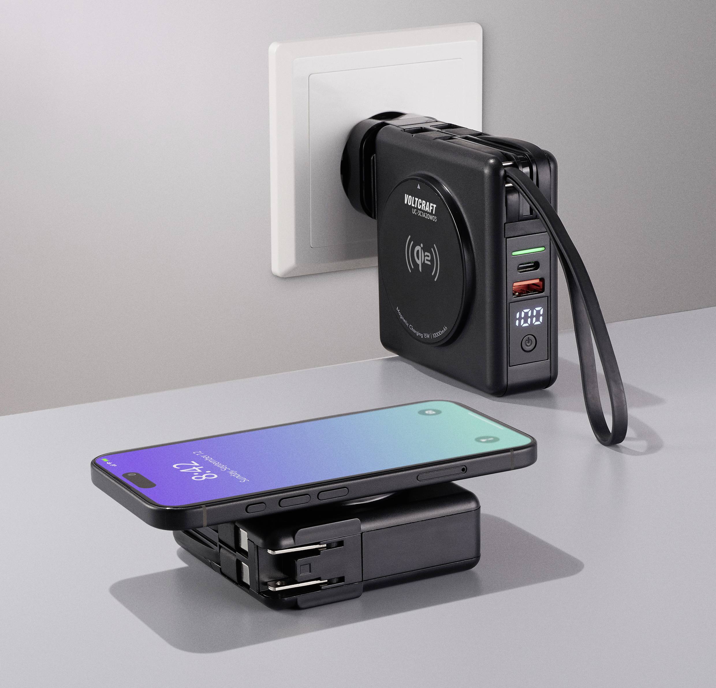 Nabíječka v elektrické zásuvce s USB porty a digitálním displejem, která bezdrátově nabíjí smartphone na stole.