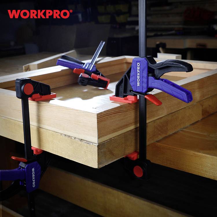 Dřevěný pracovní stůl s několika svorkami pro stabilní upevnění; na svorkách je viditelná značka 'Workpro'.