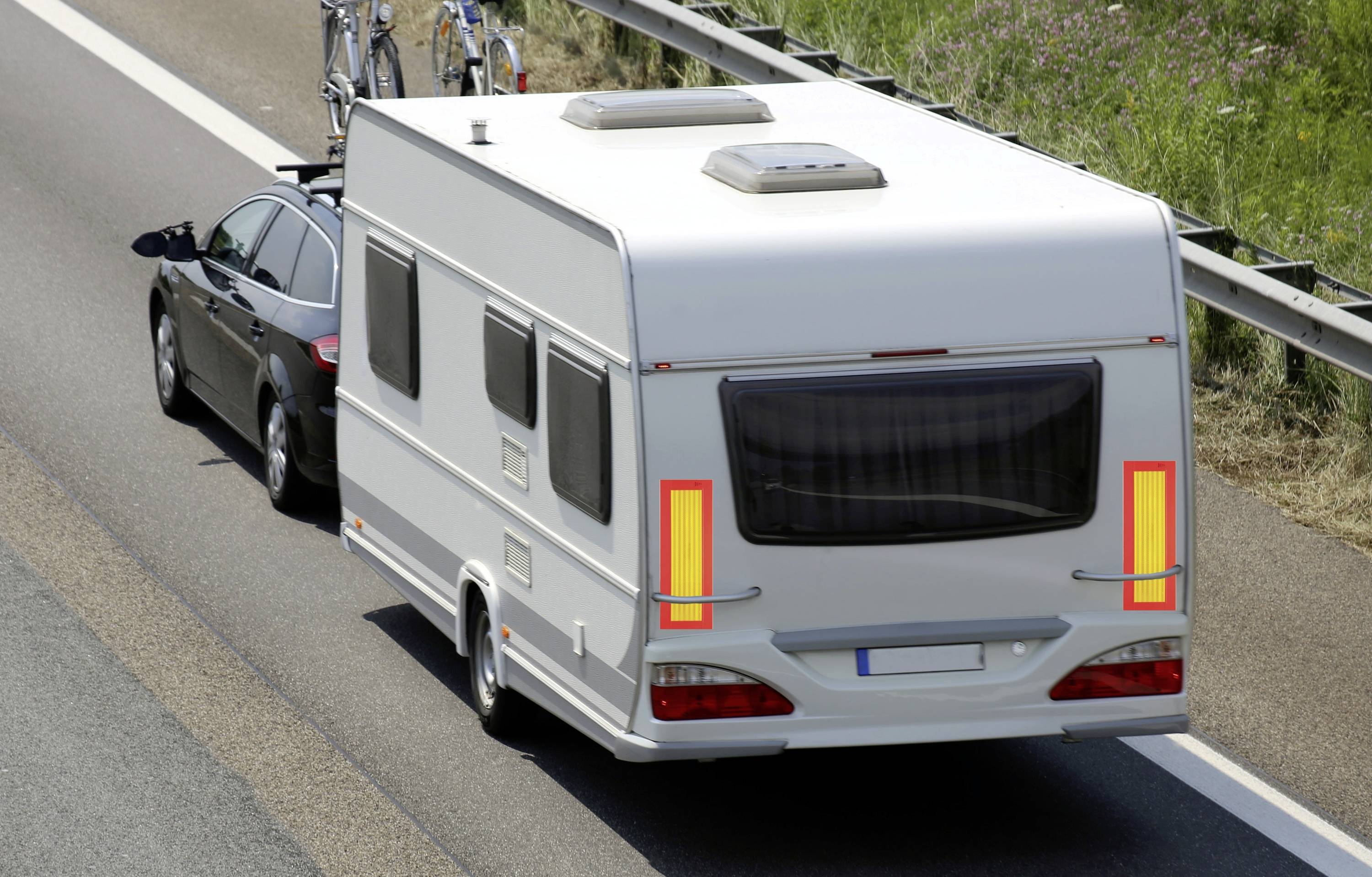 Auto táhne karavan po dálnici, jízdní kola jsou připevněna na střeše vozidla.