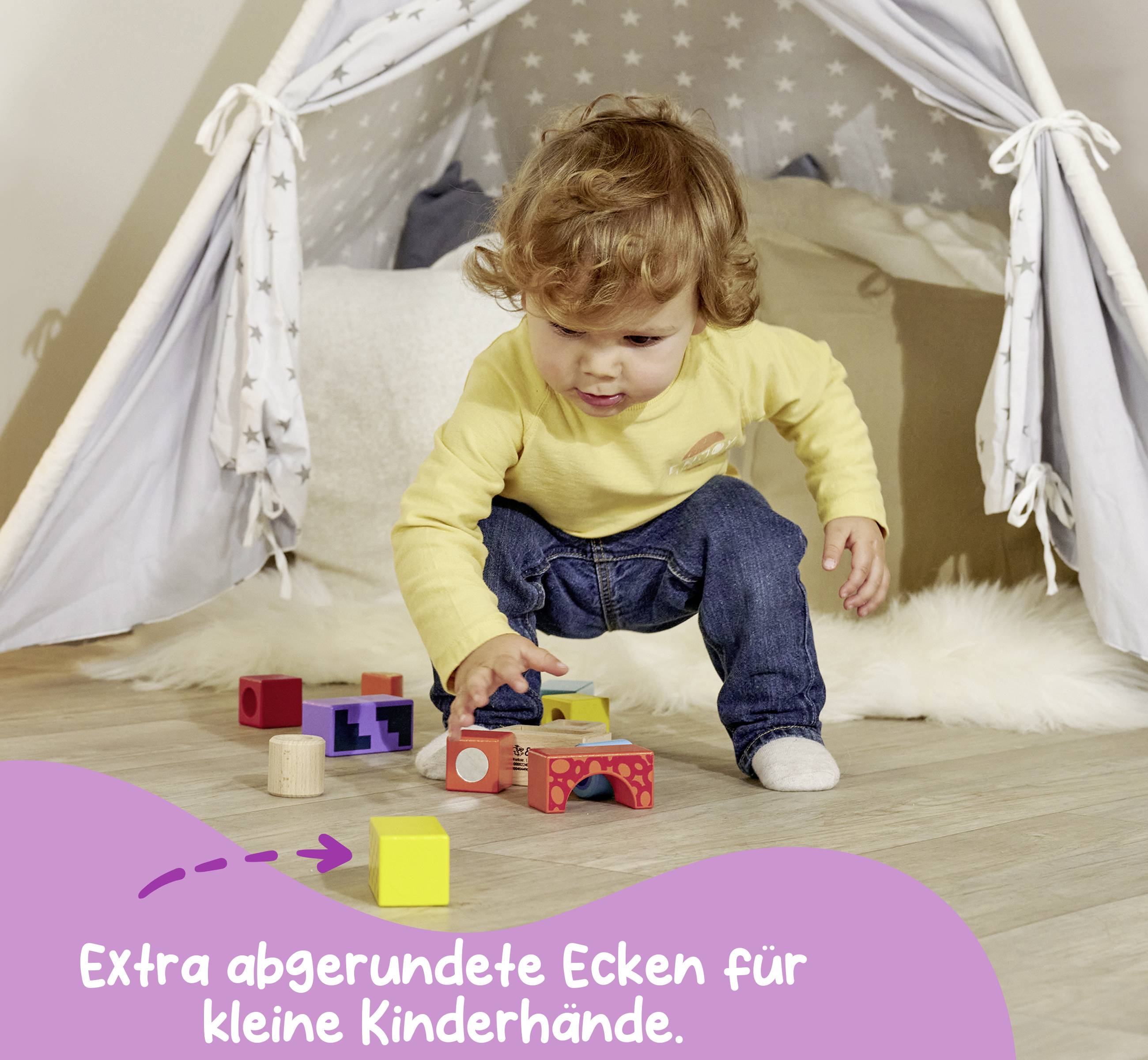 Batole si hraje s barevnými dřevěnými kostkami před zastřešeným dětským stanem. Text: 'Extra zaoblené rohy pro malé dětské ručičky.'