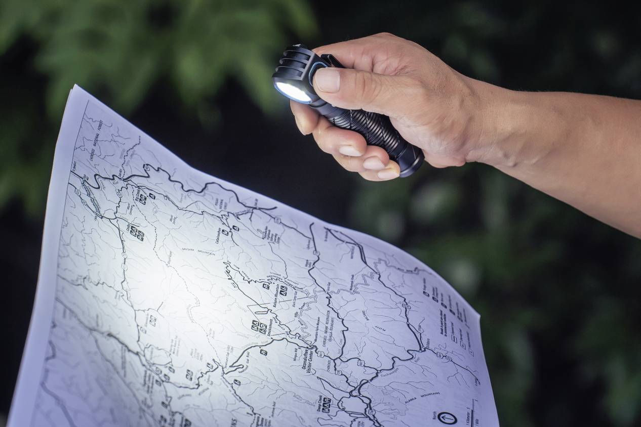 Osoba osvětluje podrobnou mapu kapesní svítilnou. Mapa zobrazuje geografické linie a místa.