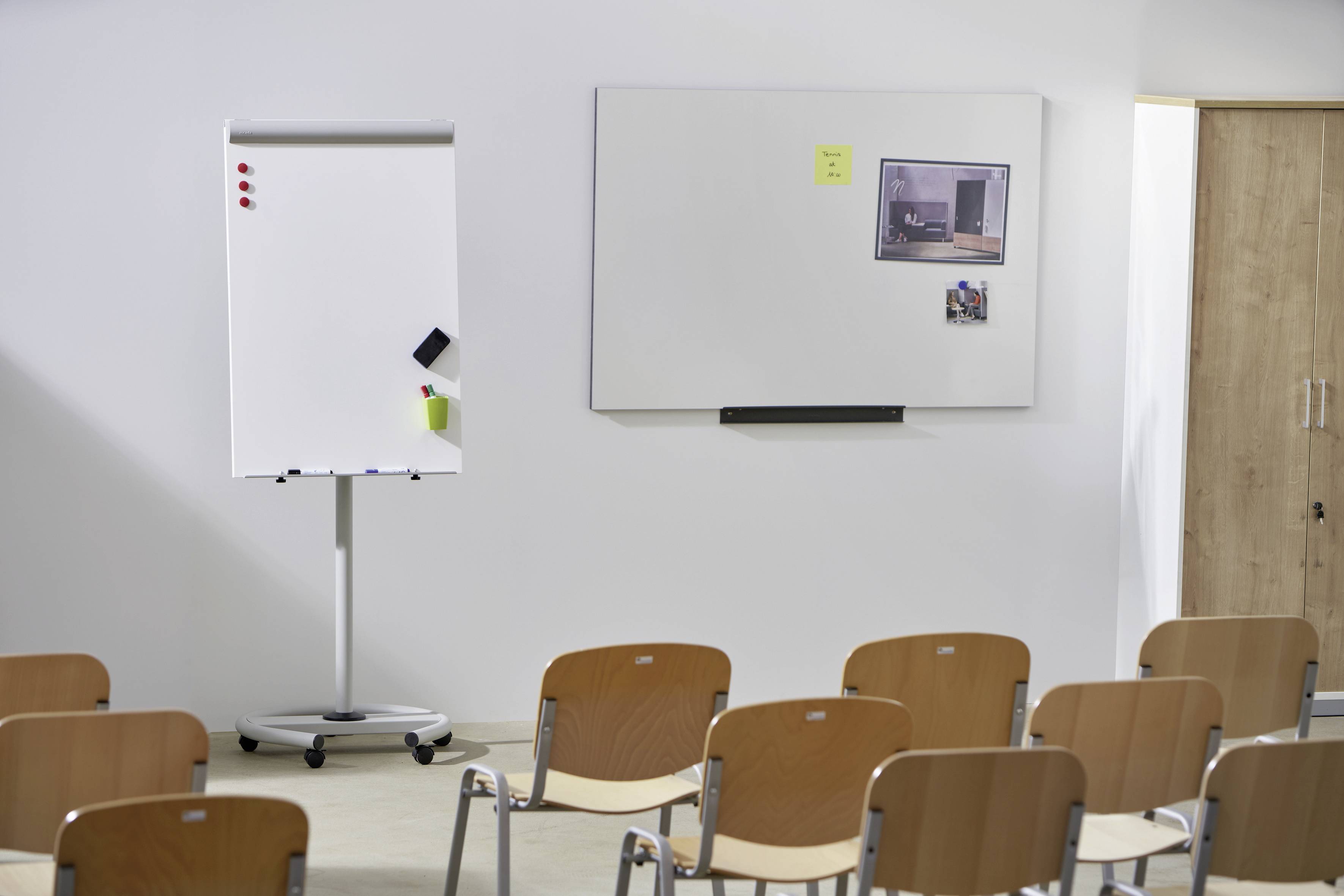 Několik řad židlí před bílou flipchartovou tabulí a nástěnnou tabulí v konferenční místnosti.