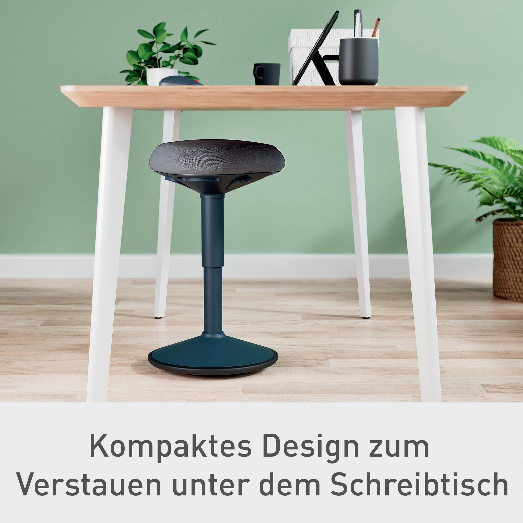 Moderní psací stůl s malou stoličkou umístěnou pod ním, obklopený rostlinami a kancelářskými potřebami. Text: 'Kompaktní design pro uskladnění pod stolem'.