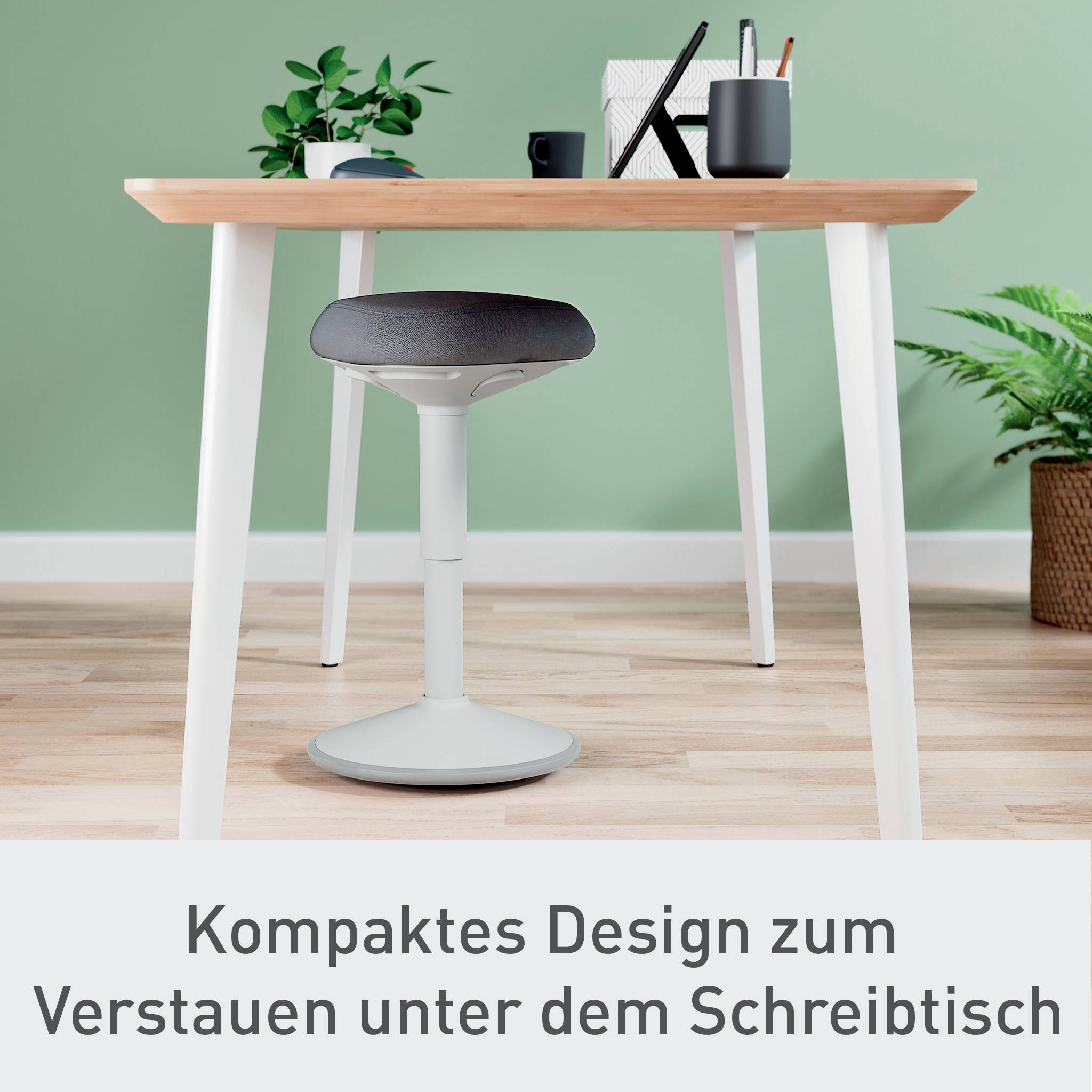 Světlý, minimalistický psací stůl s kancelářskými potřebami na něm, včetně židle se kulatým sedákem. Text dole: 'Kompaktní design pro uskladnění pod psacím stolem'.