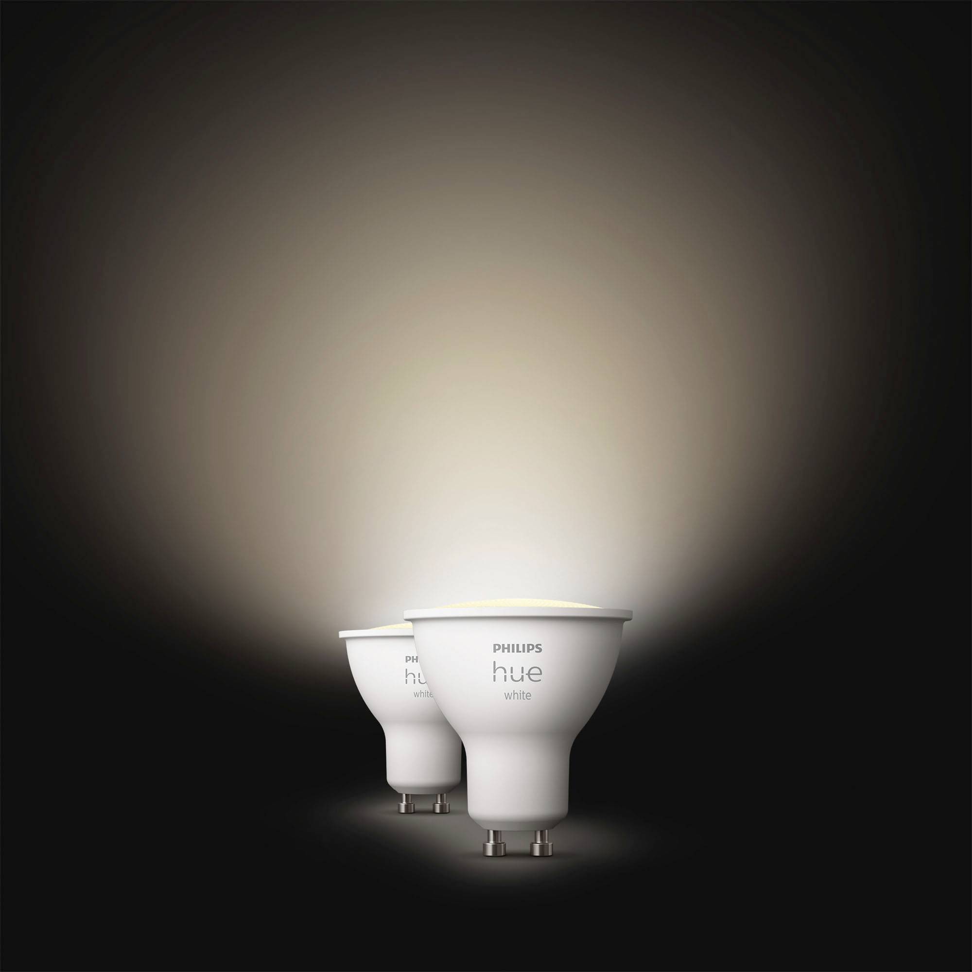 Dvě bílé LED žárovky Philips Hue GU10 svítí na tmavém pozadí, přičemž měkké světlo je vyzařováno směrem nahoru.