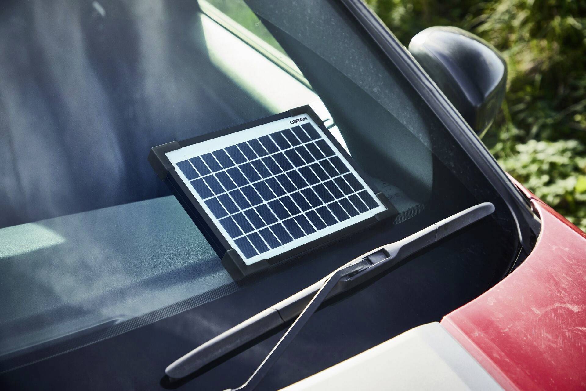 Solární panel leží na čelním skle automobilu, zjevně využíván k výrobě elektřiny pomocí slunečního světla.