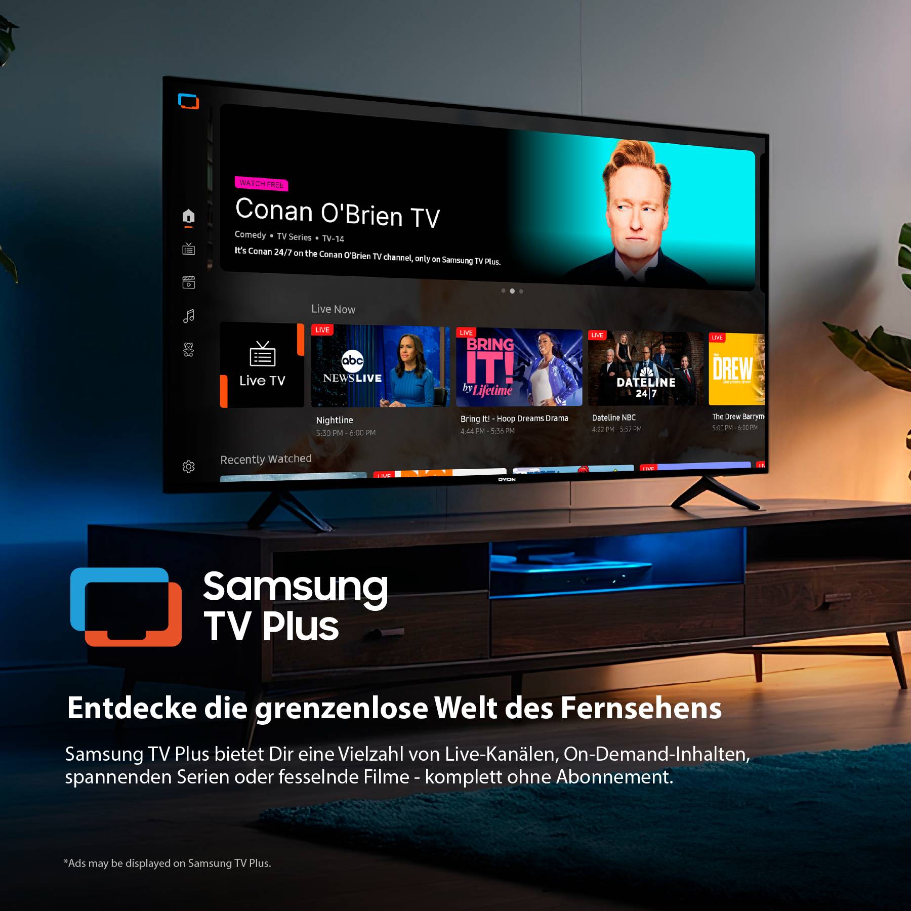 Televizor zobrazující rozhraní služby streamování s pořadem "Conan O'Brien". Logo se jmenuje "Samsung TV Plus". Jsou viditelné stůl a lampa.