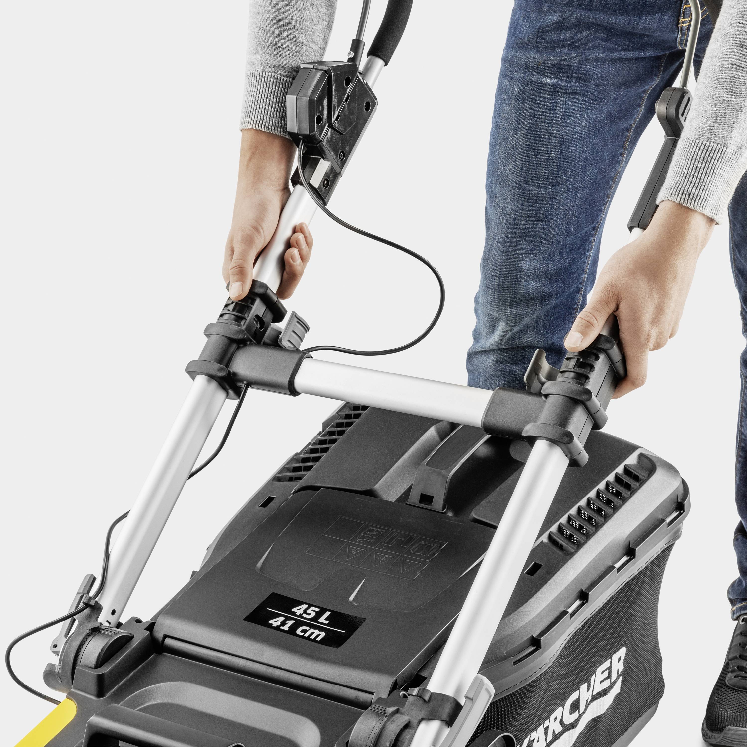 Osoba seká trávu moderním černým elektrickým sekačkou, s objemem sběrného koše 45 litrů a šířkou záběru 41 cm.