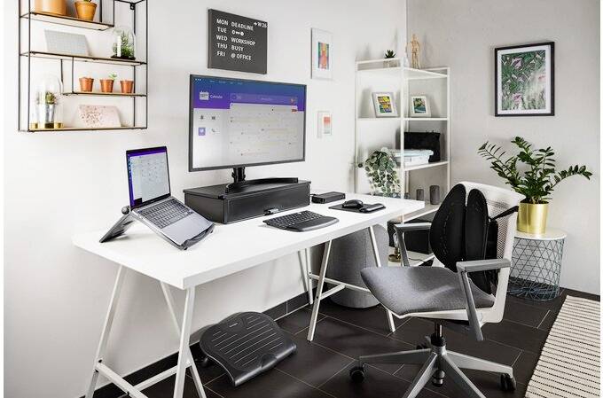 Moderní domácí kancelář s bílým stolem, dvěma monitory, laptopem, ergonomickou židlí a rostlinami jako dekorací.