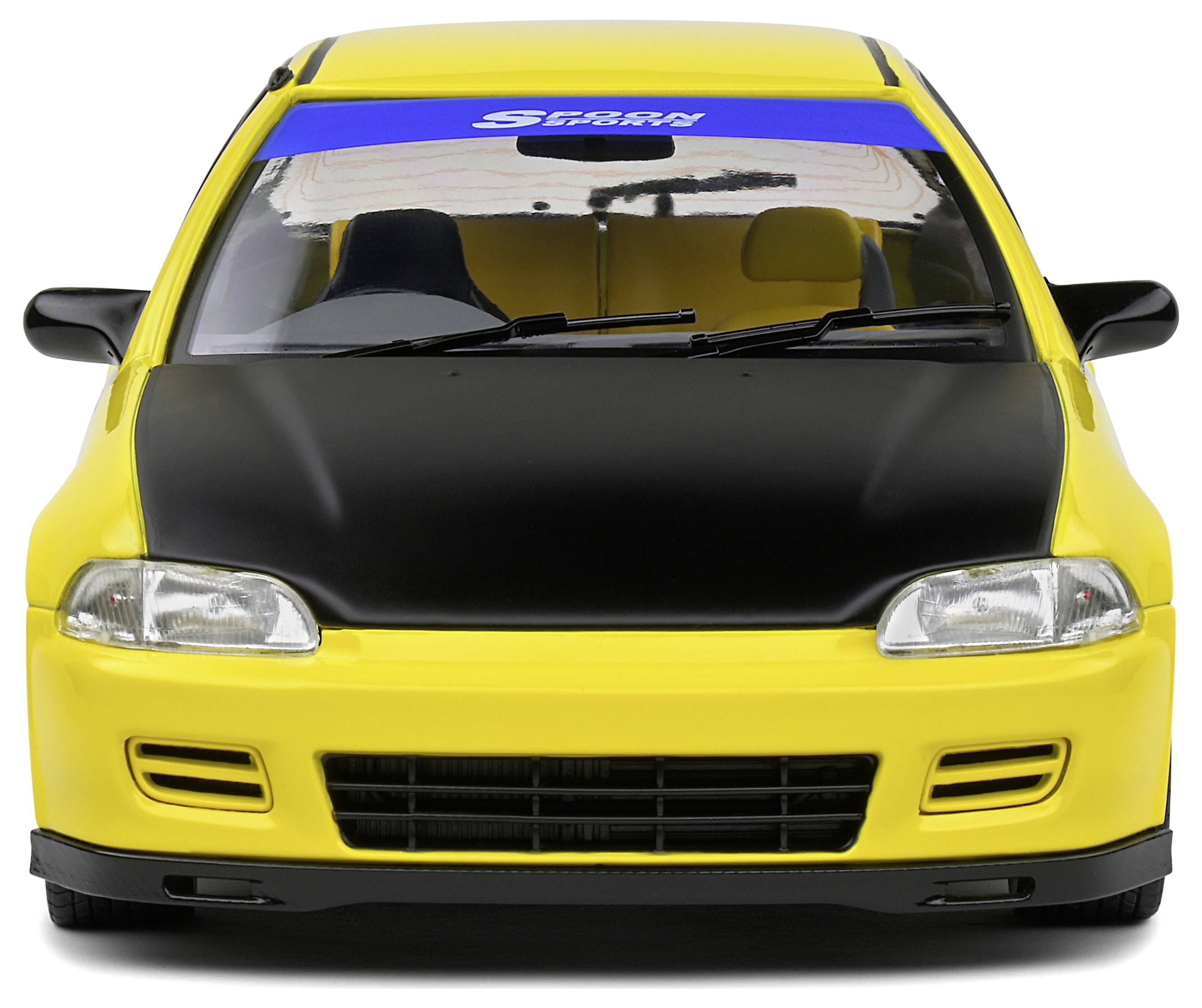 Žluté modelové auto s černou kapotou a modrým štítkem na čelním skle. Auto má sportovní vzhled.
