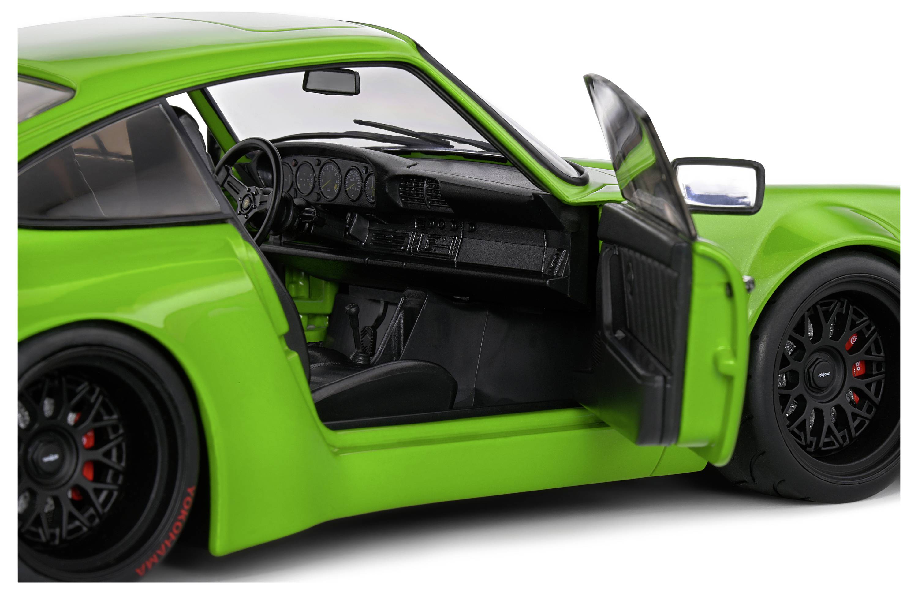 Zelené auto s otevřenými řidičovými dveřmi, černým interiérem a sportovním volantem, ukazuje moderní design a sportovní charakter.