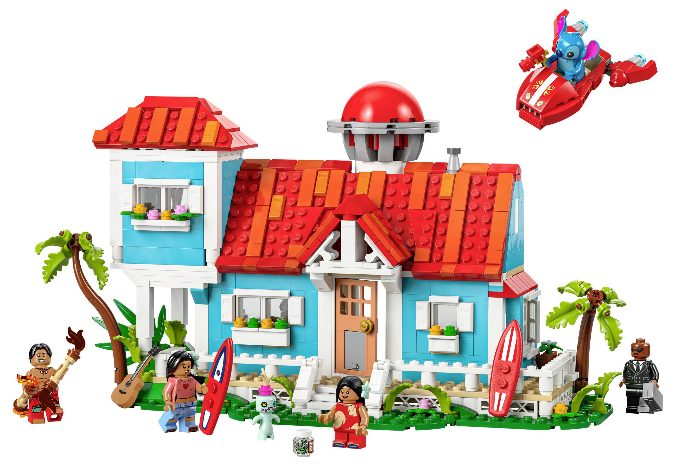 Barevný LEGO dům na pláži s červenými střechami, surfovými prkny a palmou. Nahoře vpravo letí malá modrá figurka v červeném létajícím stroji.
