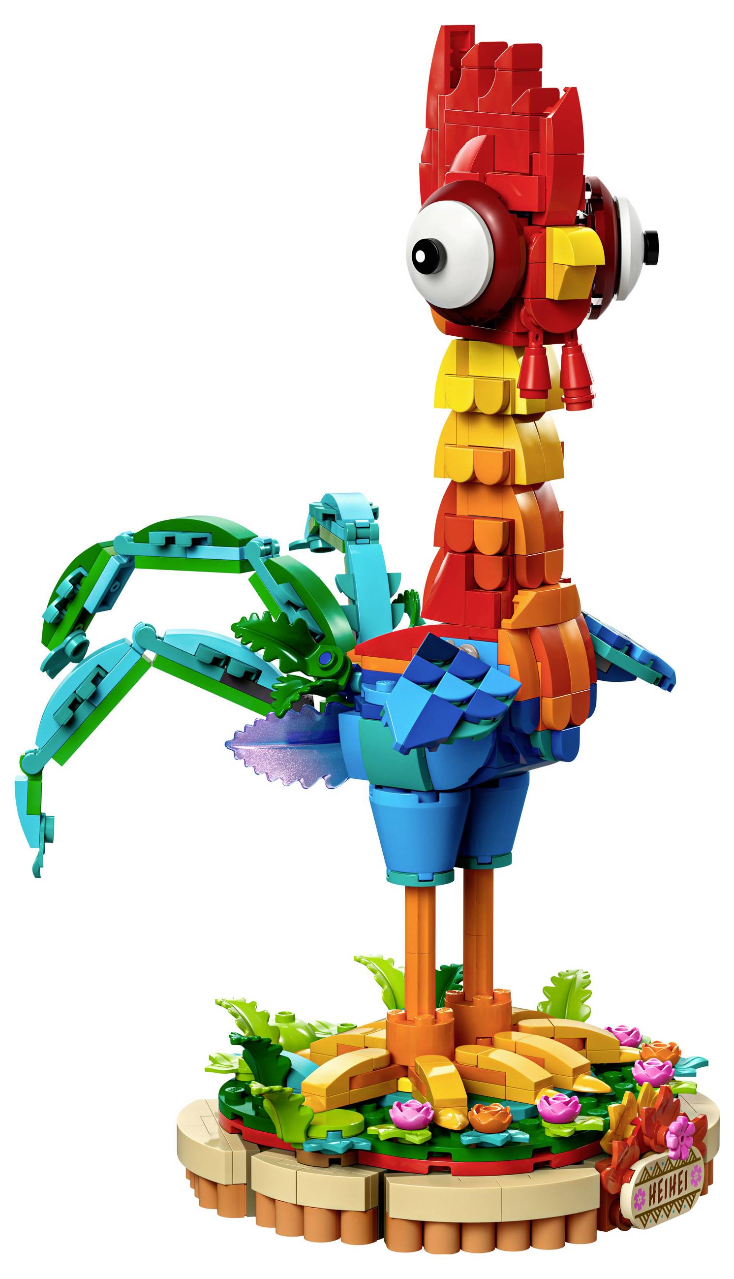 Barevný LEGO model stojícího kohouta s velkýma očima, pestrobarevným peřím a zeleným ocasem, obklopený květinami na podstavci.