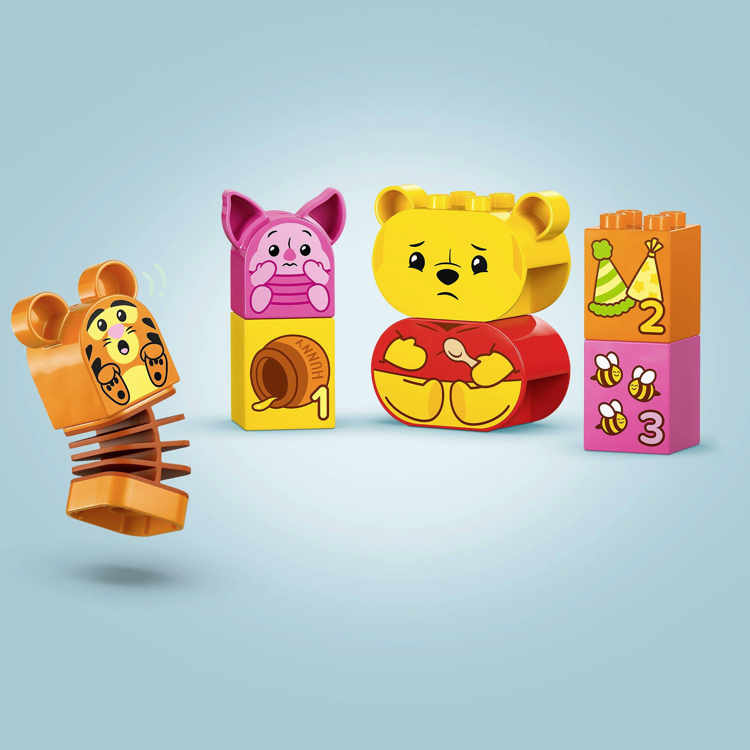 Tři LEGO kostky s motivy medvědů, očíslované barevnými oblečky, šnekem a číselnými symboly 1-3 na modrém pozadí.
