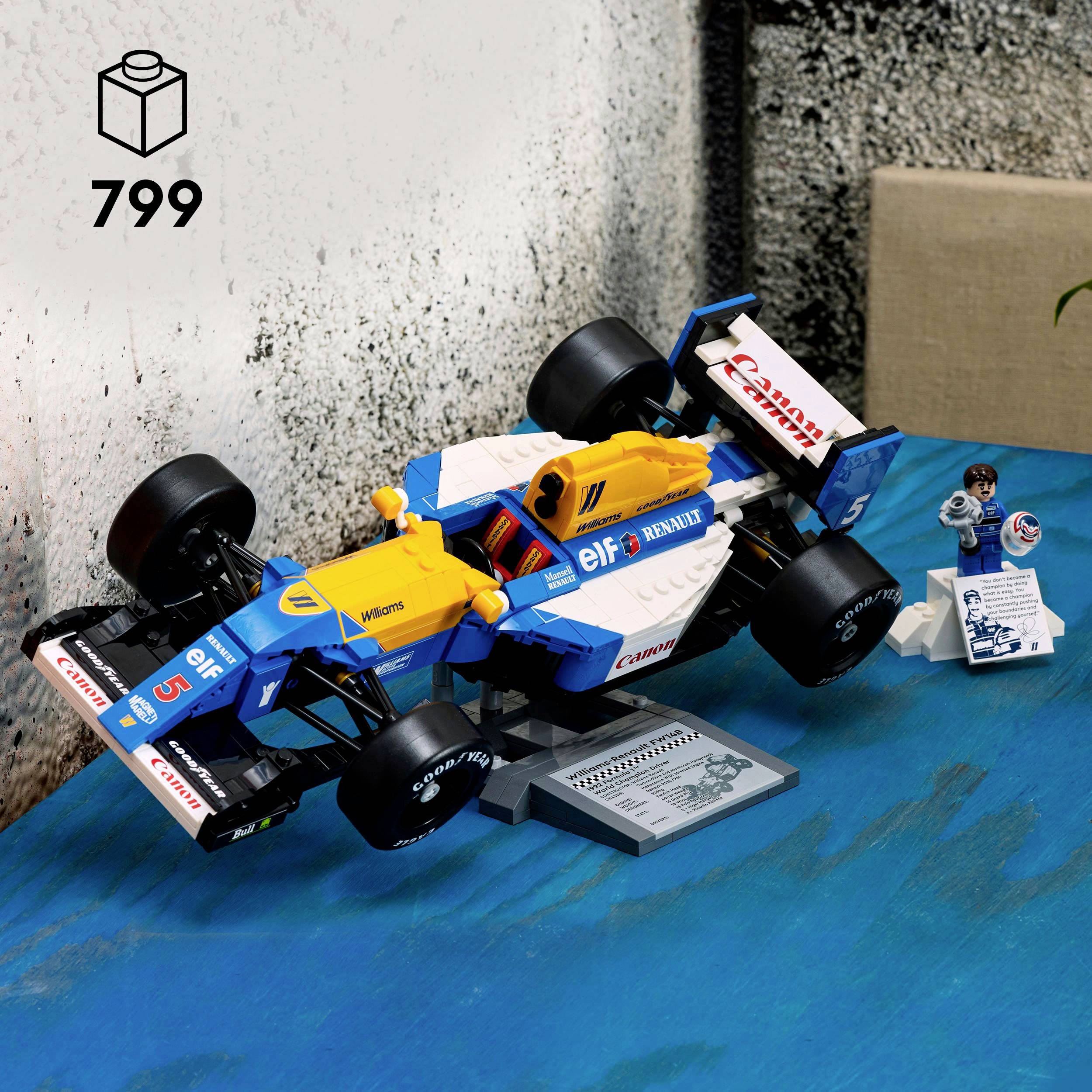 Barevné modelové auto na modrém stole, které připomíná formuli 1 složenou z lego kostek, s oficiální krabicí znázorňující sadu '799'.