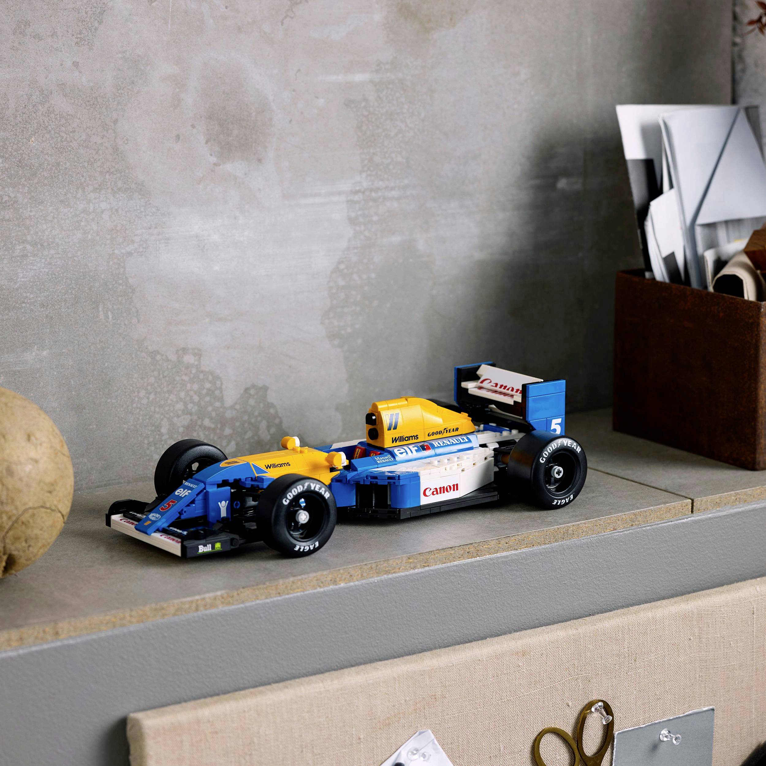 Detailní model formule 1 stojí na poličce vedle stojanu s roztříděnými obálkami.