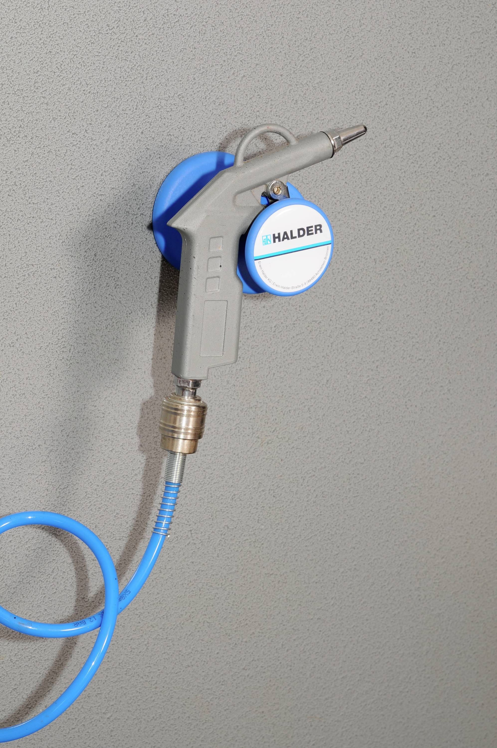 Modrá pneumatická pistole visí na držáku na šedé zdi. Modré spirálové vedení propojuje pistoli s držákem.