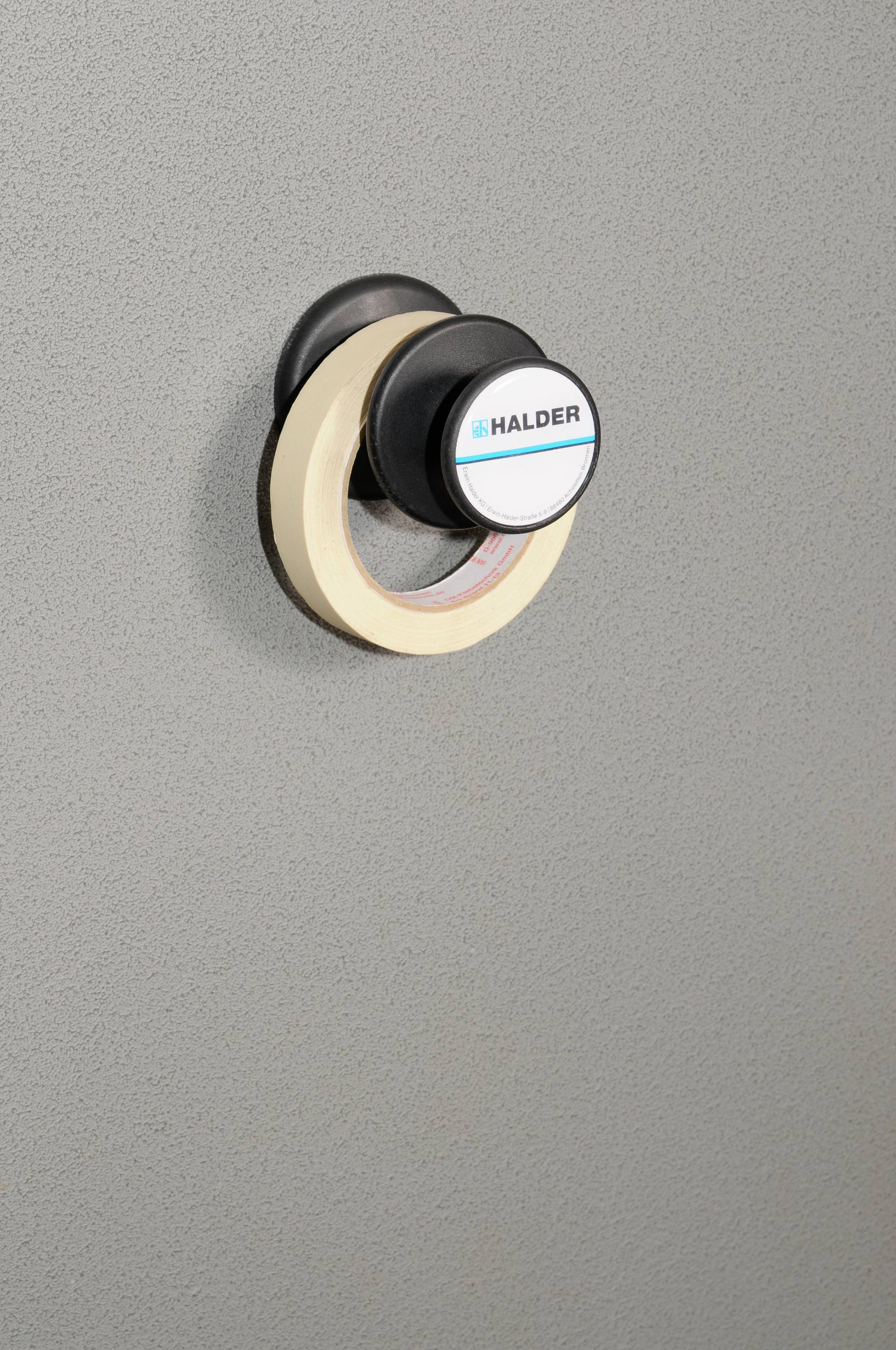 Kulatý dveřní doraz s černým a béžovým plastovým pouzdrem na šedém pozadí, s vytištěným názvem značky 'Halder'.