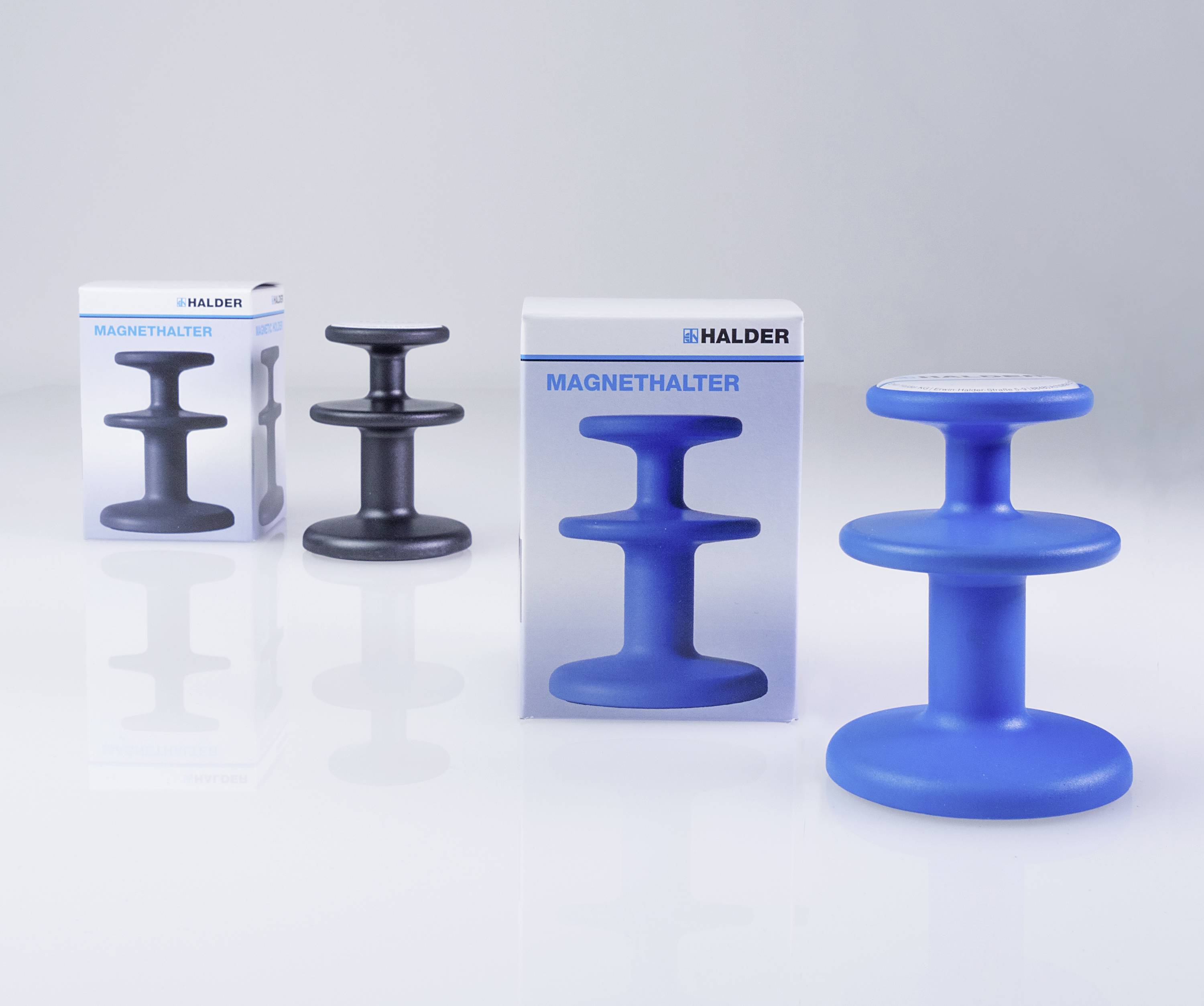 Tři kulaté magnetické držáky na hladkém povrchu, v modré a černé barvě. Balení s nápisem 'Magnetické držáky' od firmy Halder.