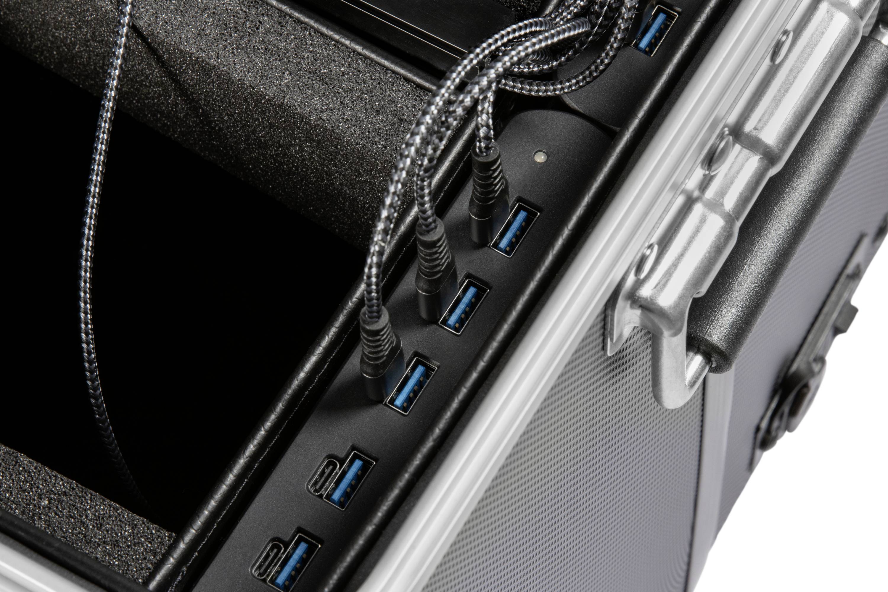 Stříbrný kufřík s několika zapojenými černými kabely do USB portů. Kabely jsou opletené a lesklé.