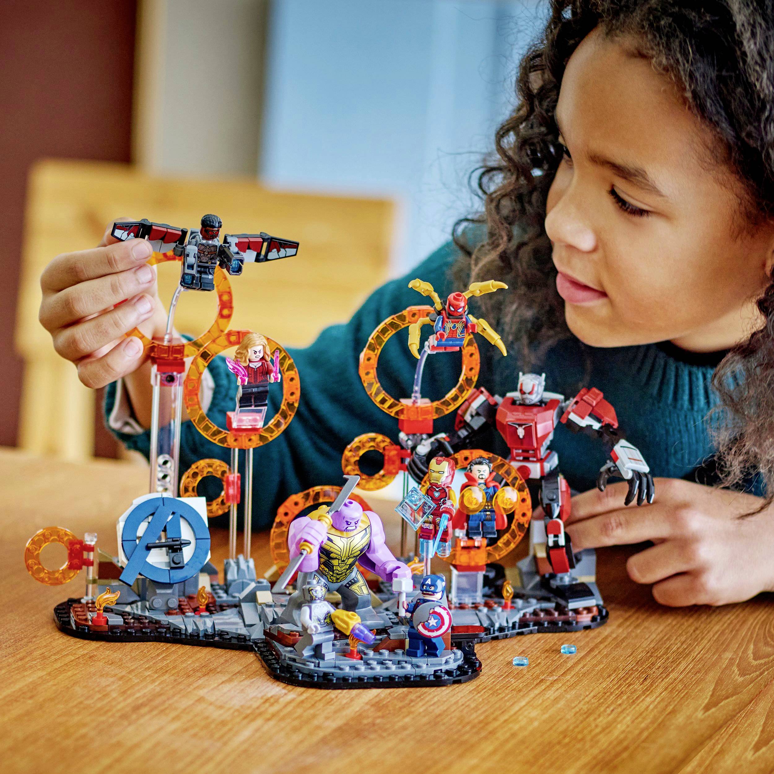 Dítě si hraje se sadou 'Lego Avengers'. Jsou zde viditelné postavy jako Iron Man a Thanos, obklopené barevnými stavebními díly.