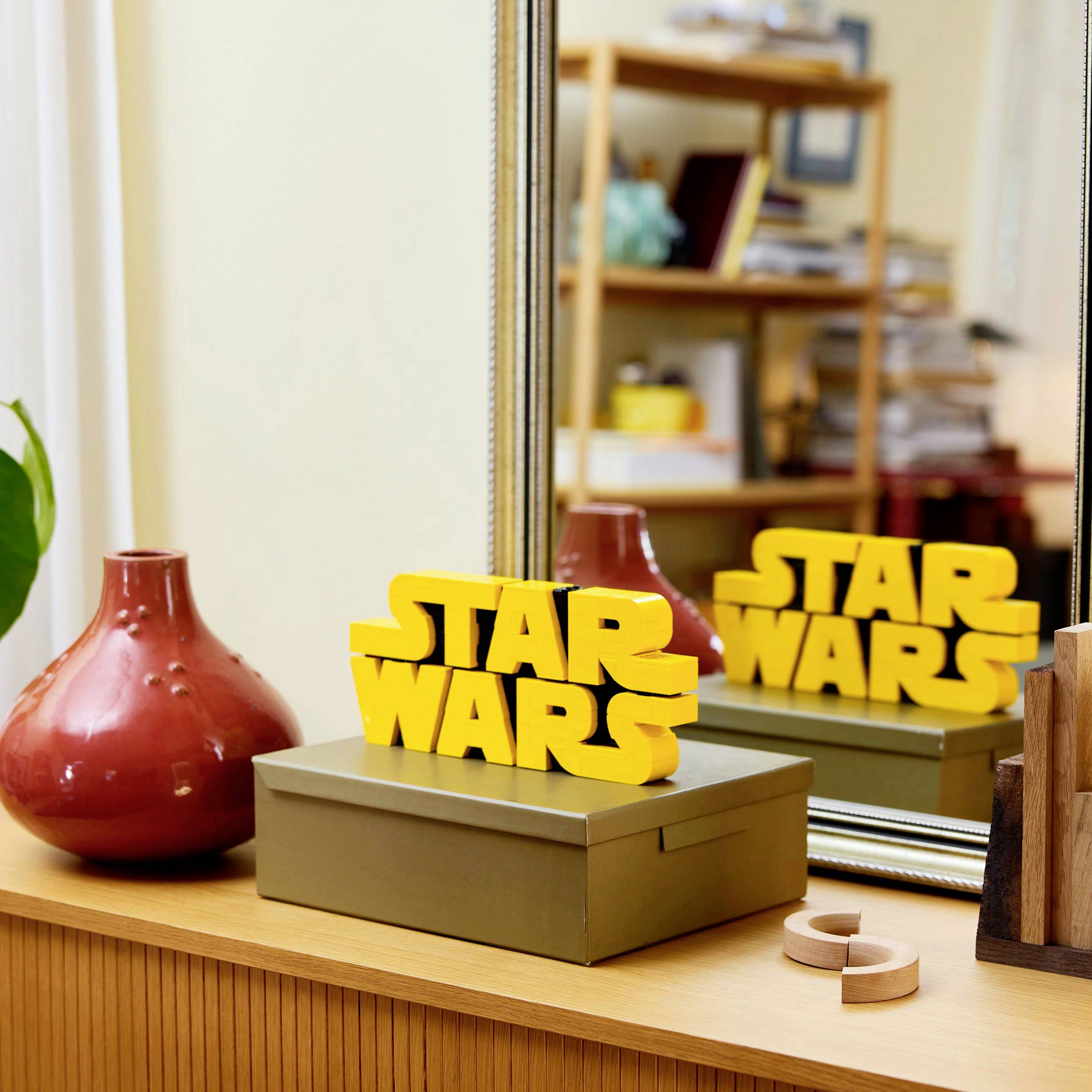 Žlutý nápis "Star Wars" na stole před zrcadlem, které odráží knihovnu v pozadí.