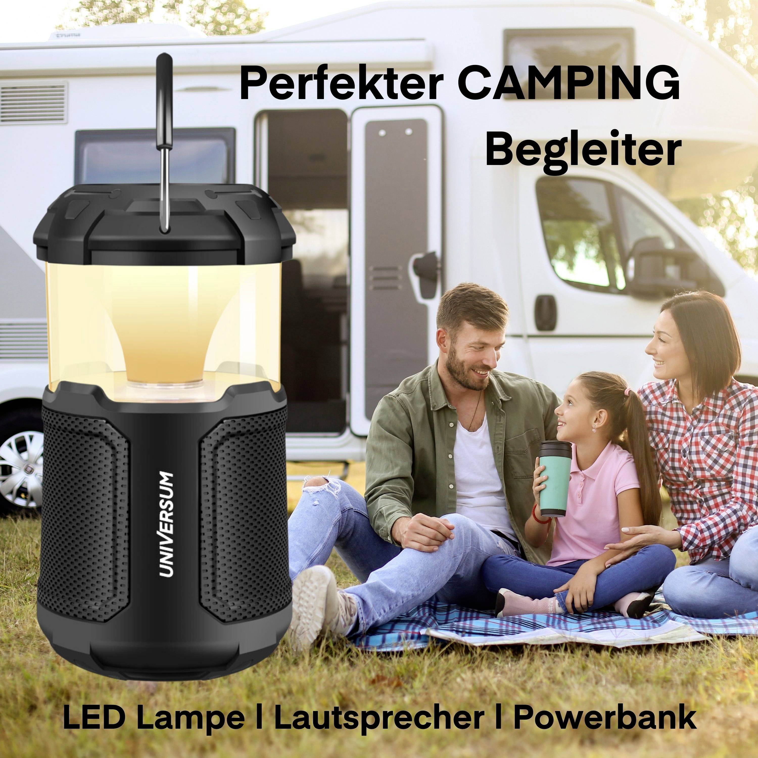 Rodina odpočívá v kempovací zóně před obytným vozem. V popředí stojí LED lampa s nápisem 'Universum'. Text: 'Perfektní KEMPOVÝ společník. LED lampa | Reproduktor | Powerbanka'.