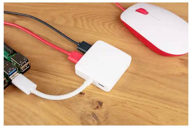 Raspberry Pi s připojenými kabely, červenou a bílou počítačovou myší a bílým adaptérem na dřevěném stole.