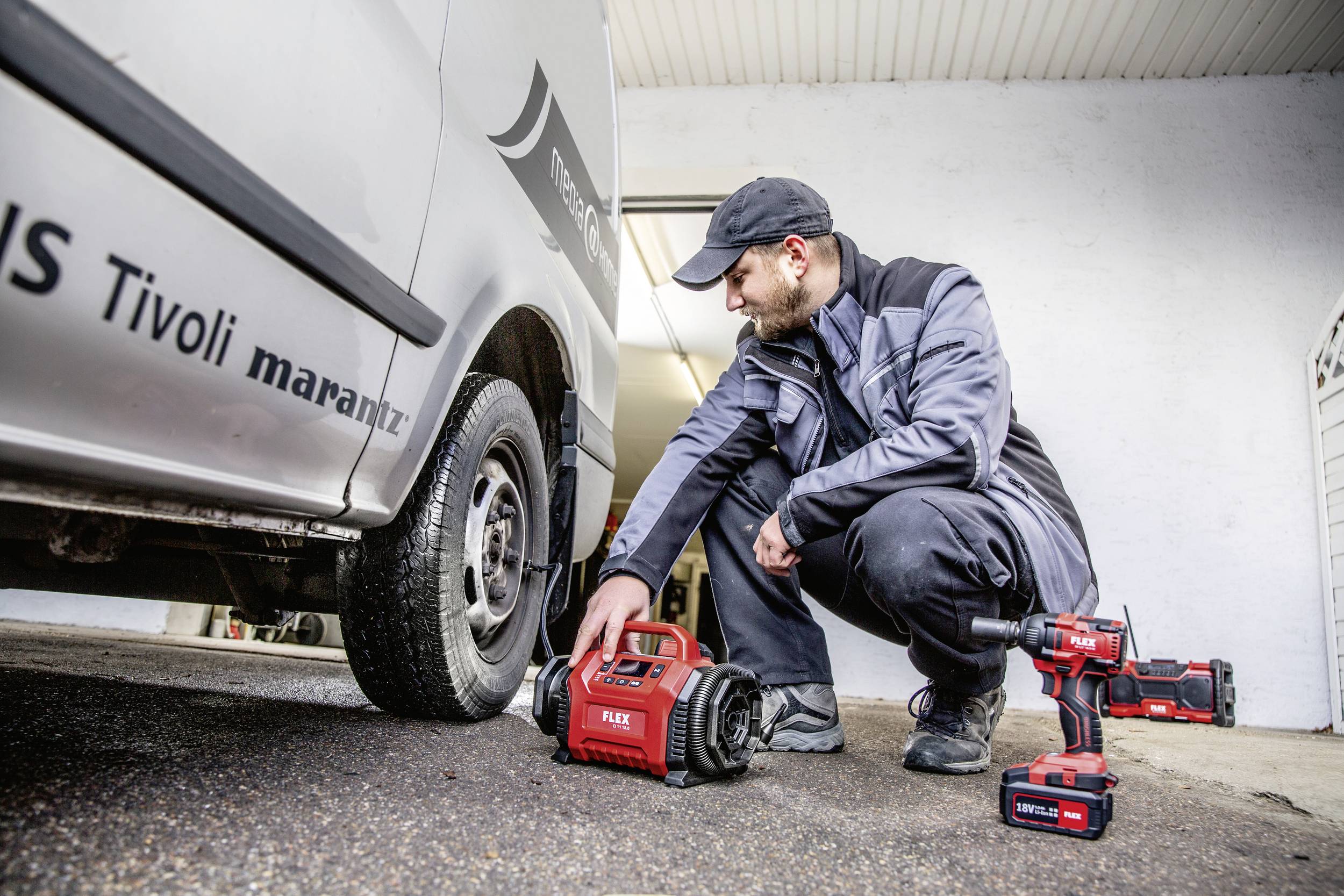 Mechanik kontroluje tlak vzduchu v pneumatice dodávky pomocí přenosného kompresoru. Vedle leží montážní kufřík a akumulátorový šroubovák.