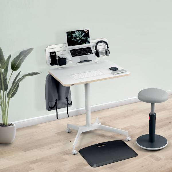 Moderní psací stůl s laptopem, sluchátky a rostlinami. Vedle stojí ergonomická stolička a podložka na podlahu. Ideální pro home office.