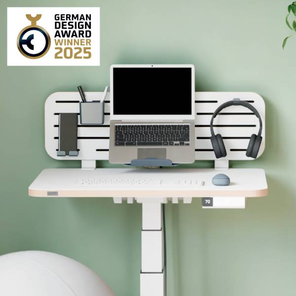 Moderní výškově nastavitelný psací stůl s laptopem, sluchátky a příslušenstvím. Vítěz German Design Award 2025.