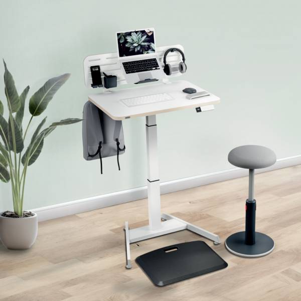 Výškově nastavitelný psací stůl s laptopem, sluchátky a rostlinami, vedle něj ergonomická stolička, na světlé dřevěné podlaze.