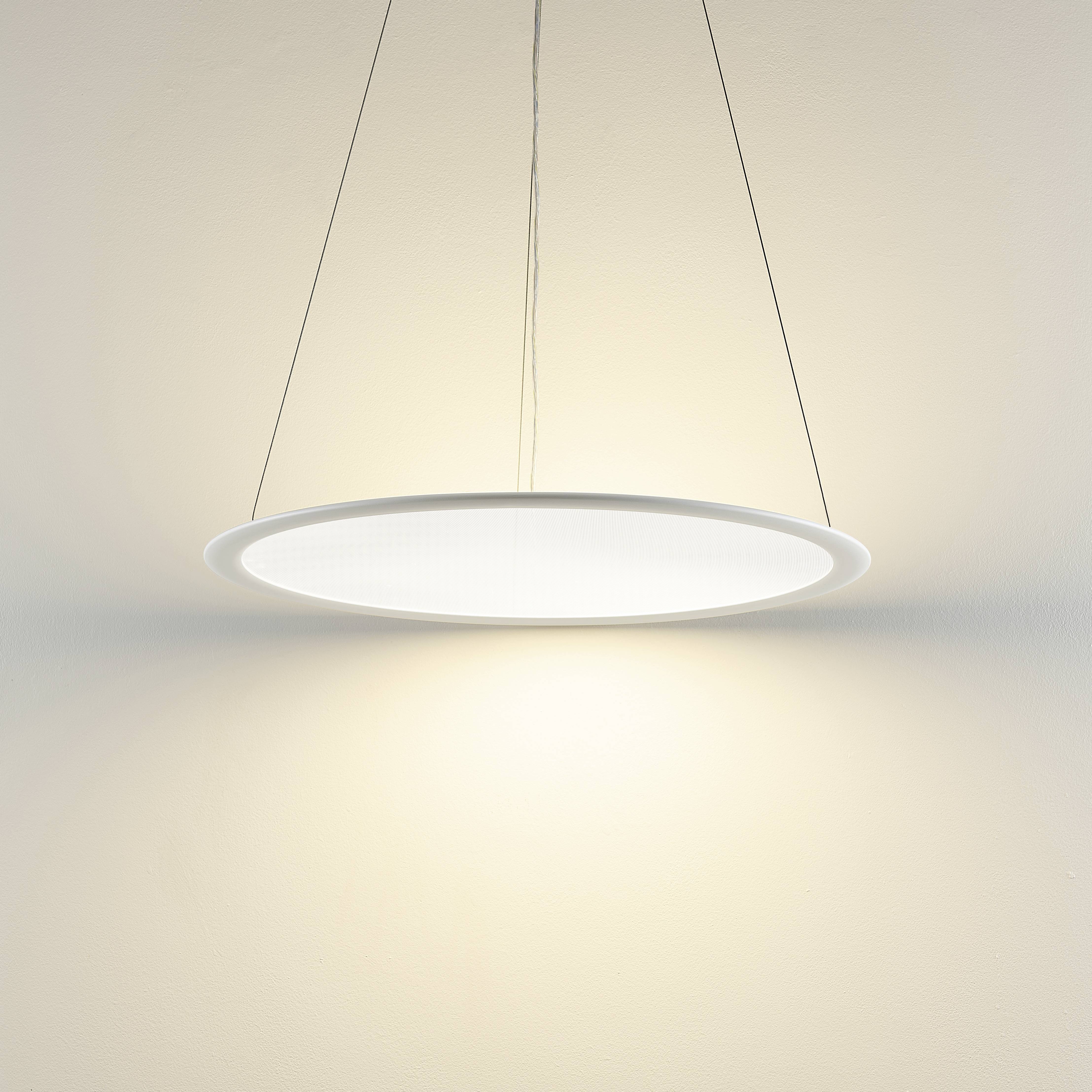 Moderní, kulatá stropní lampa z bílého materiálu, zavěšená, jasně svítí v jednoduchém prostoru.