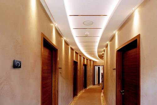 Elegantní chodba s moderními dřevěnými dveřmi, měkkým osvětlením na stropě a stěnách, které vytvářejí teplou atmosféru.