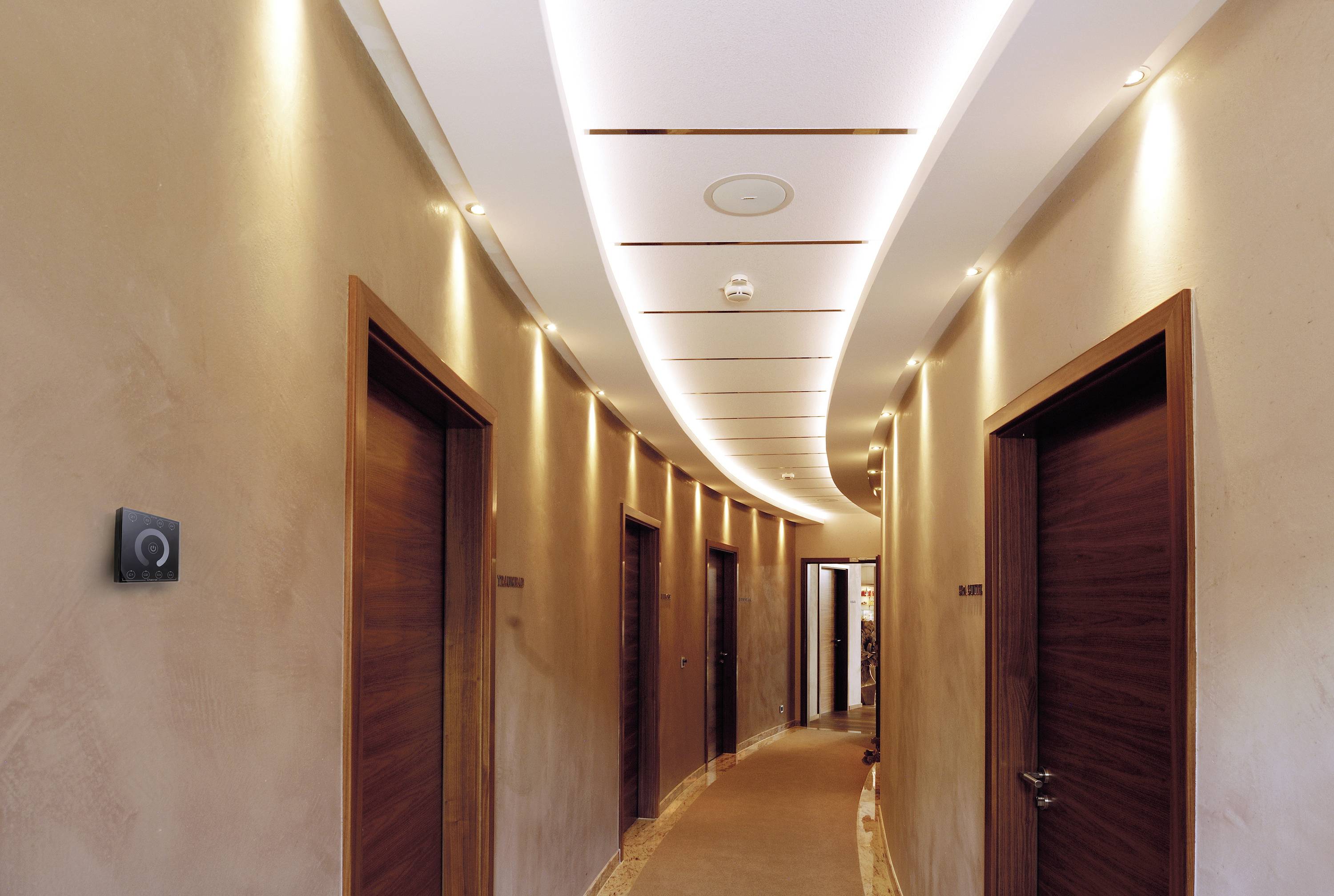 Elegantní hotelová chodba s několika dřevěnými dveřmi a moderním stropním osvětlením vedoucí do pozadí.