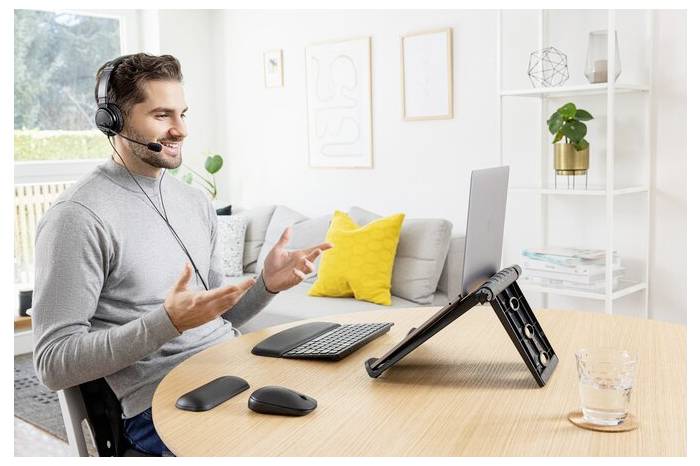 Muž pracuje z domova na laptopu a mluví přes headset. Místnost je světlá a moderně zařízená.