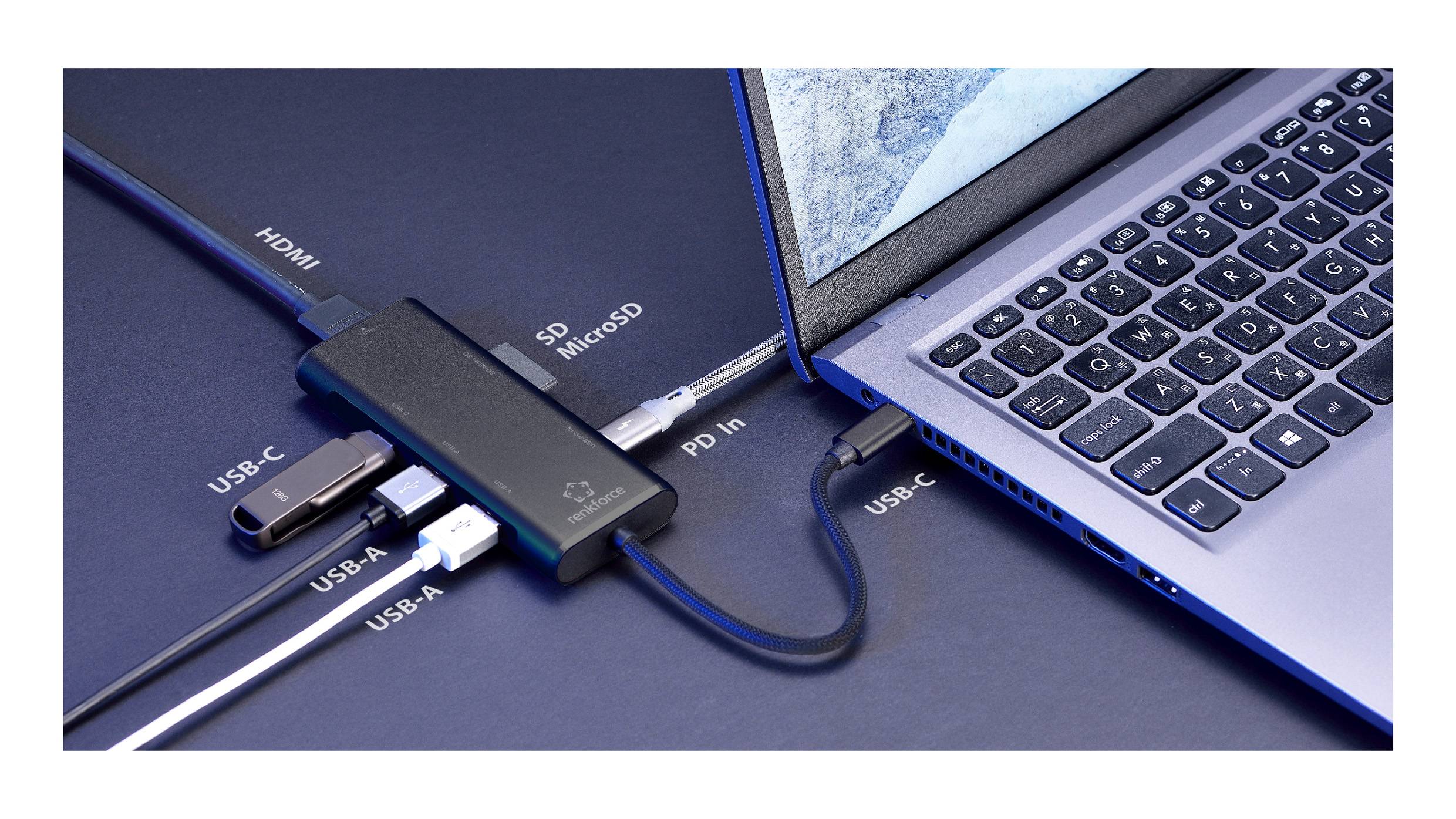 Laptop je připojen k multiportovému rozbočovači. Rozbočovač obsahuje porty HDMI, USB-C, USB-A a čtečku karet, přičemž každé připojení je označeno štítkem.