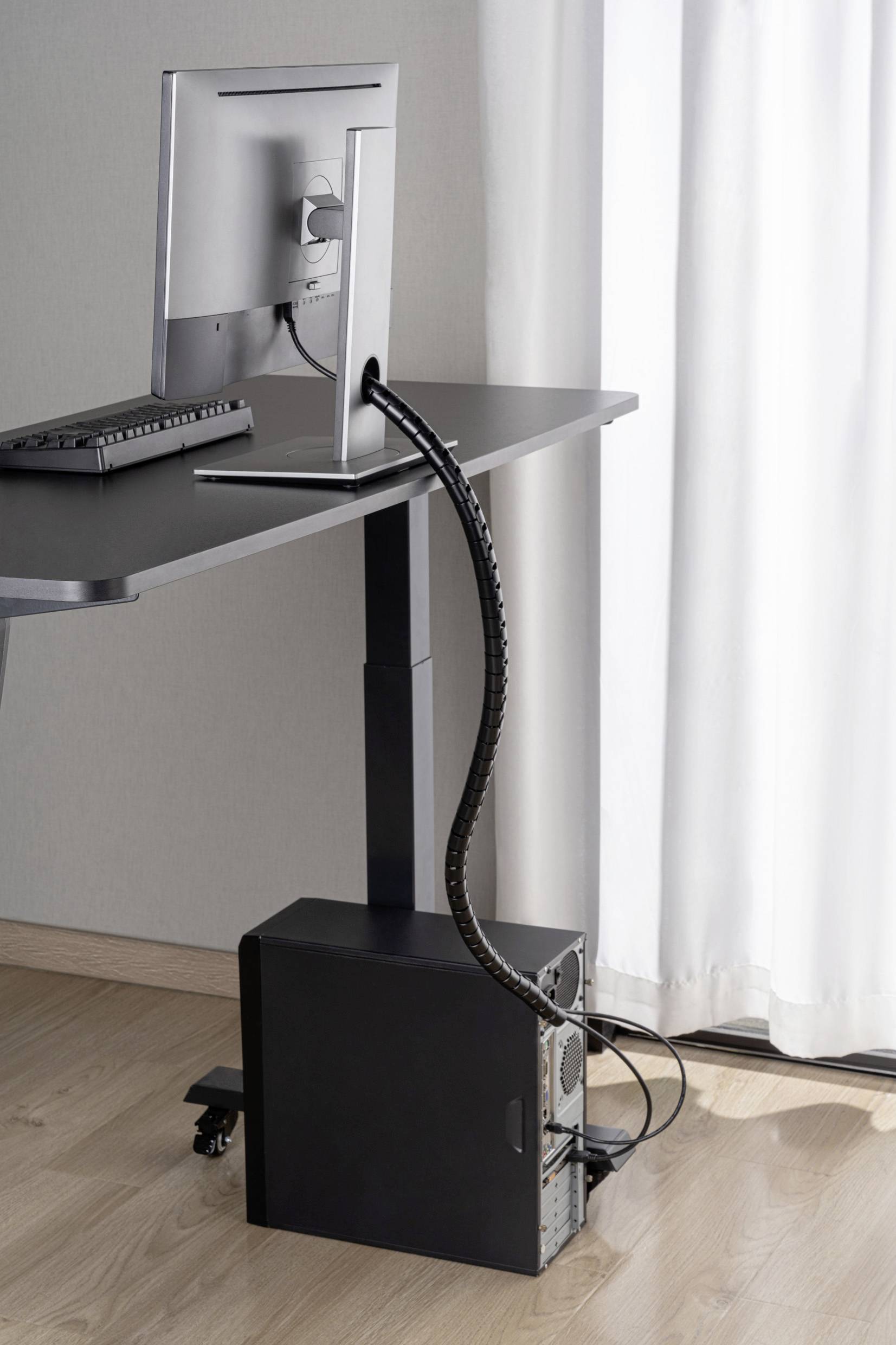 Psací stůl s funkcí nastavení výšky. Na stole je umístěn počítač s monitorem. Kabely jsou uloženy v pořádku.