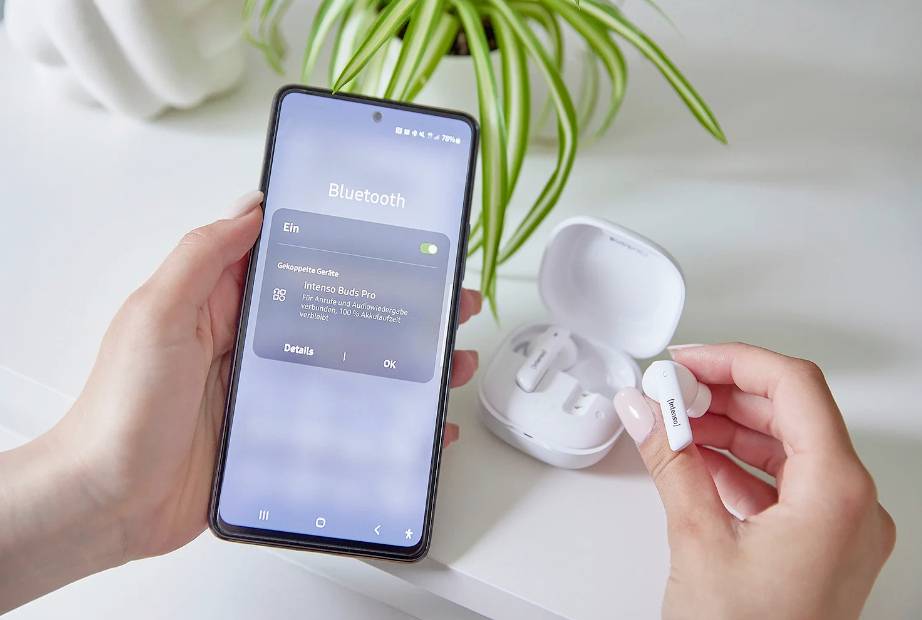 Osoba připojuje bezdrátová sluchátka ke smartphonu pomocí Bluetooth. Sluchátka jsou v nabíjecím pouzdře a smartphone zobrazuje stav připojení.