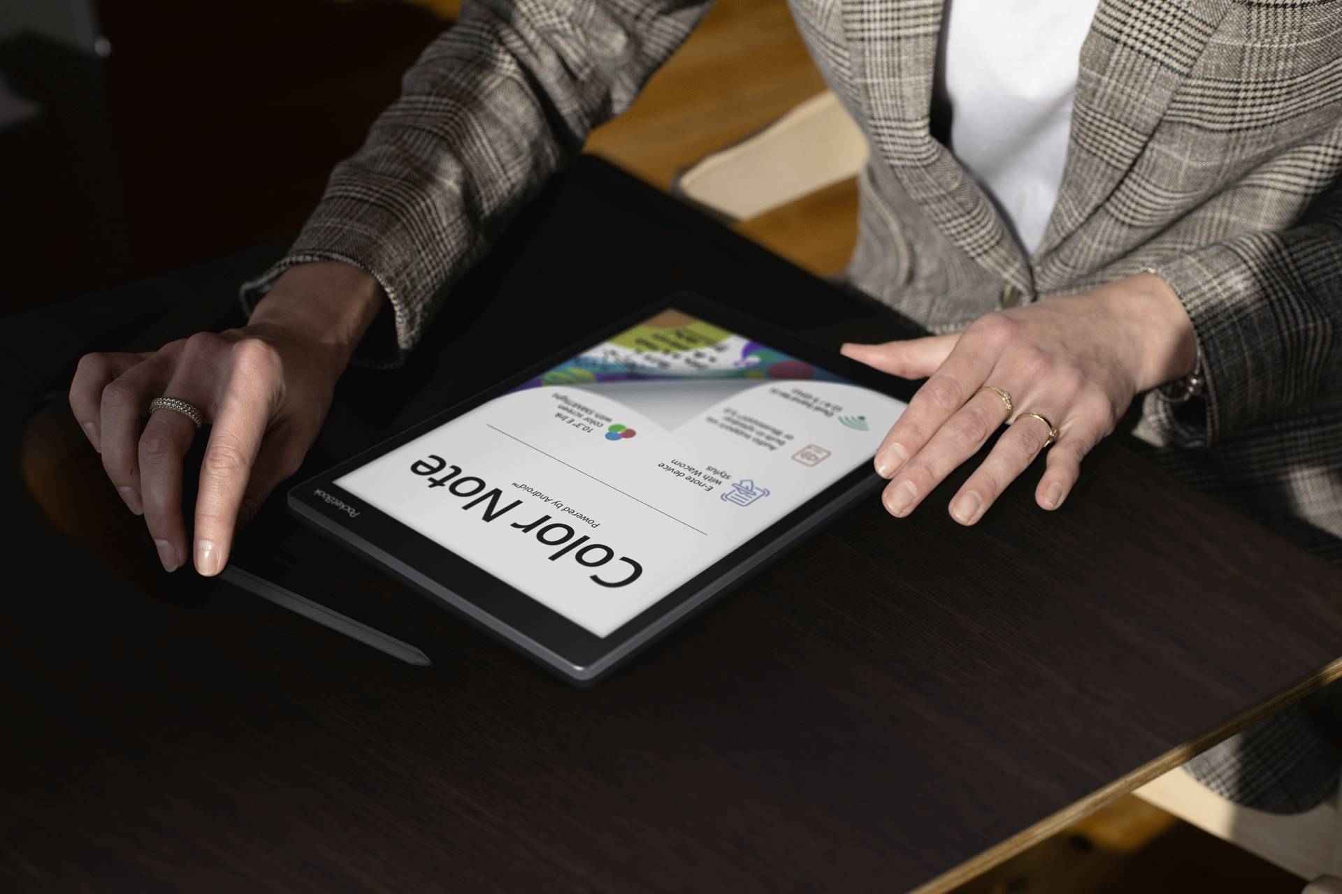 Osoba sedící u stolu drží tablet-pero vedle tabletu zobrazujícího aplikaci 'Color Note'.