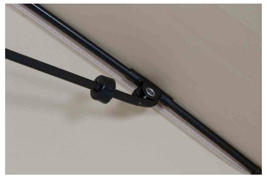 Černá páka je připevněná na kolejnici u stropu, pravděpodobně součást mechanického systému pro pohyb nebo stabilizaci.