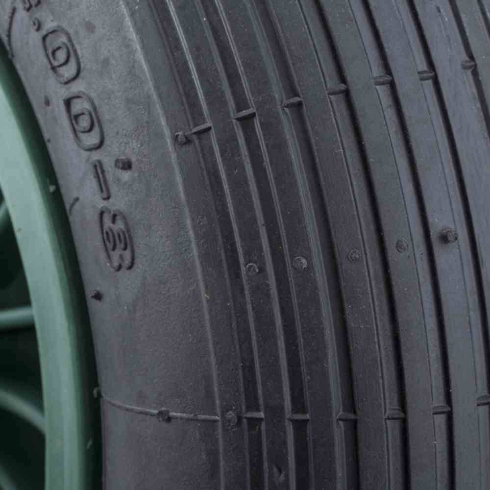 Detailní záběr pneumatiky automobilu s viditelným vzorkem dezénu. Pneumatika je namontována na zelené ráfku.