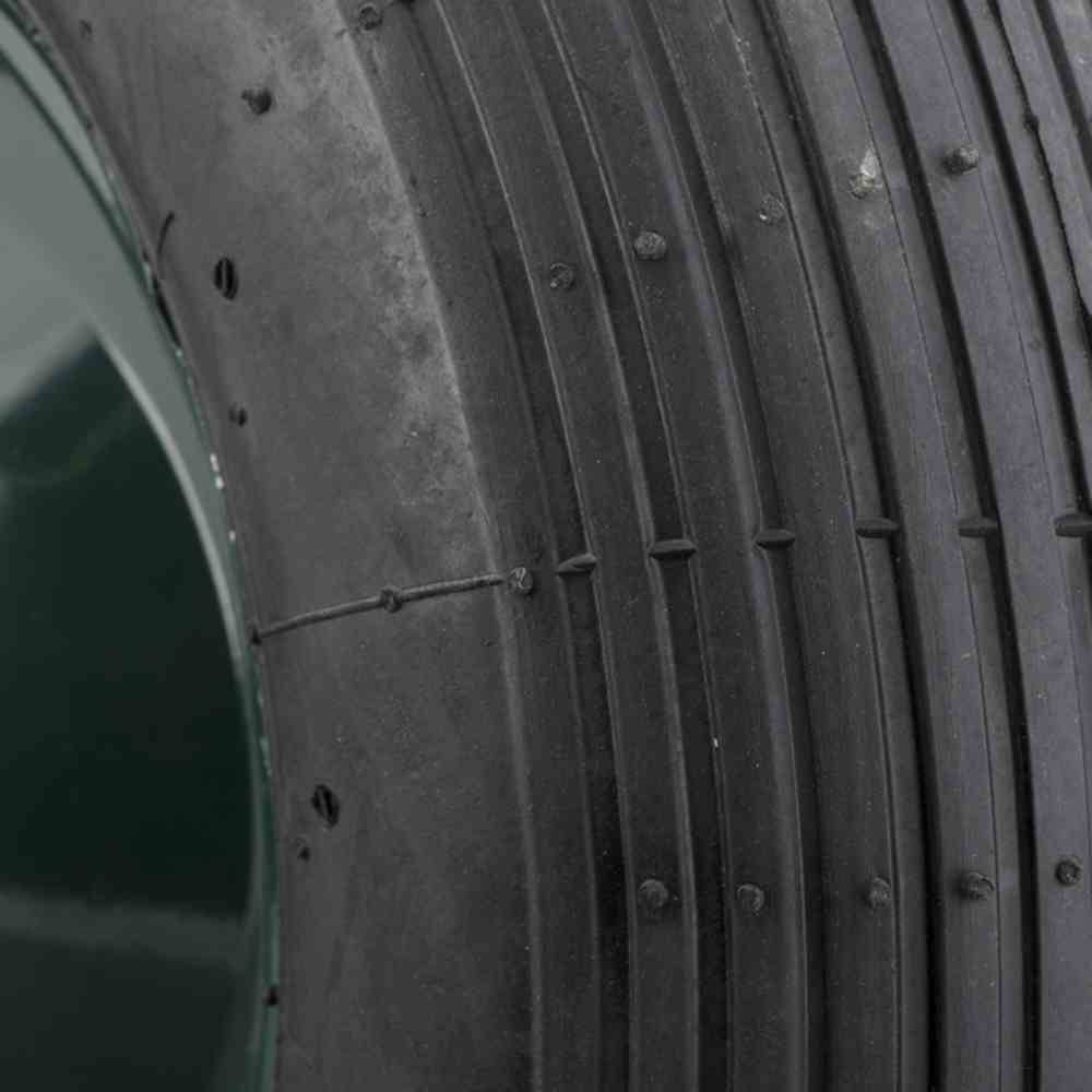 Detailní záběr dezénu pneumatiky s úzkými drážkami a hladkým povrchem, vhodný pro asfaltové silnice nebo závodní okruhy.