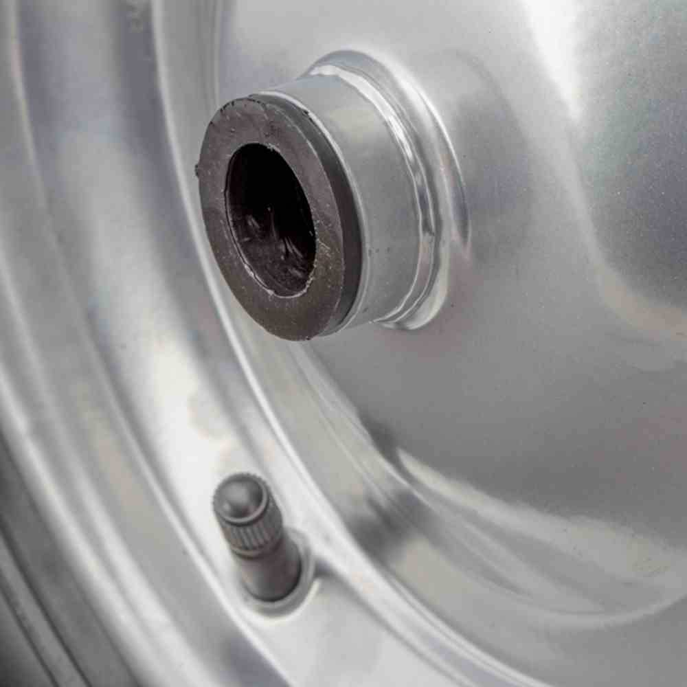 Detailní záběr stříbrného automobilového kola s ventilem a šroubem kola uprostřed.