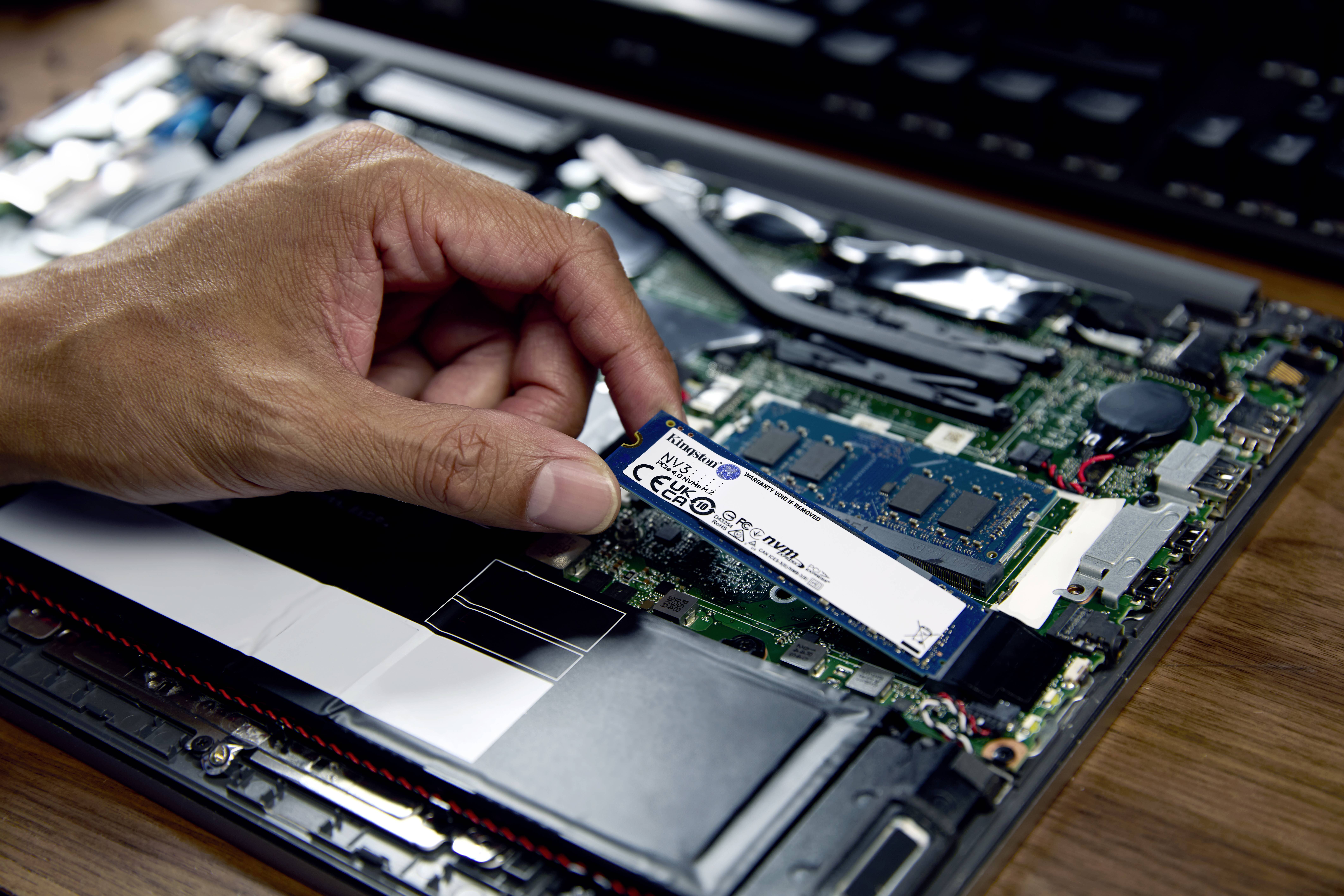Ruka vkládá M.2 SSD do laptopového počítače. Základní deska a paměťové moduly RAM jsou viditelné.