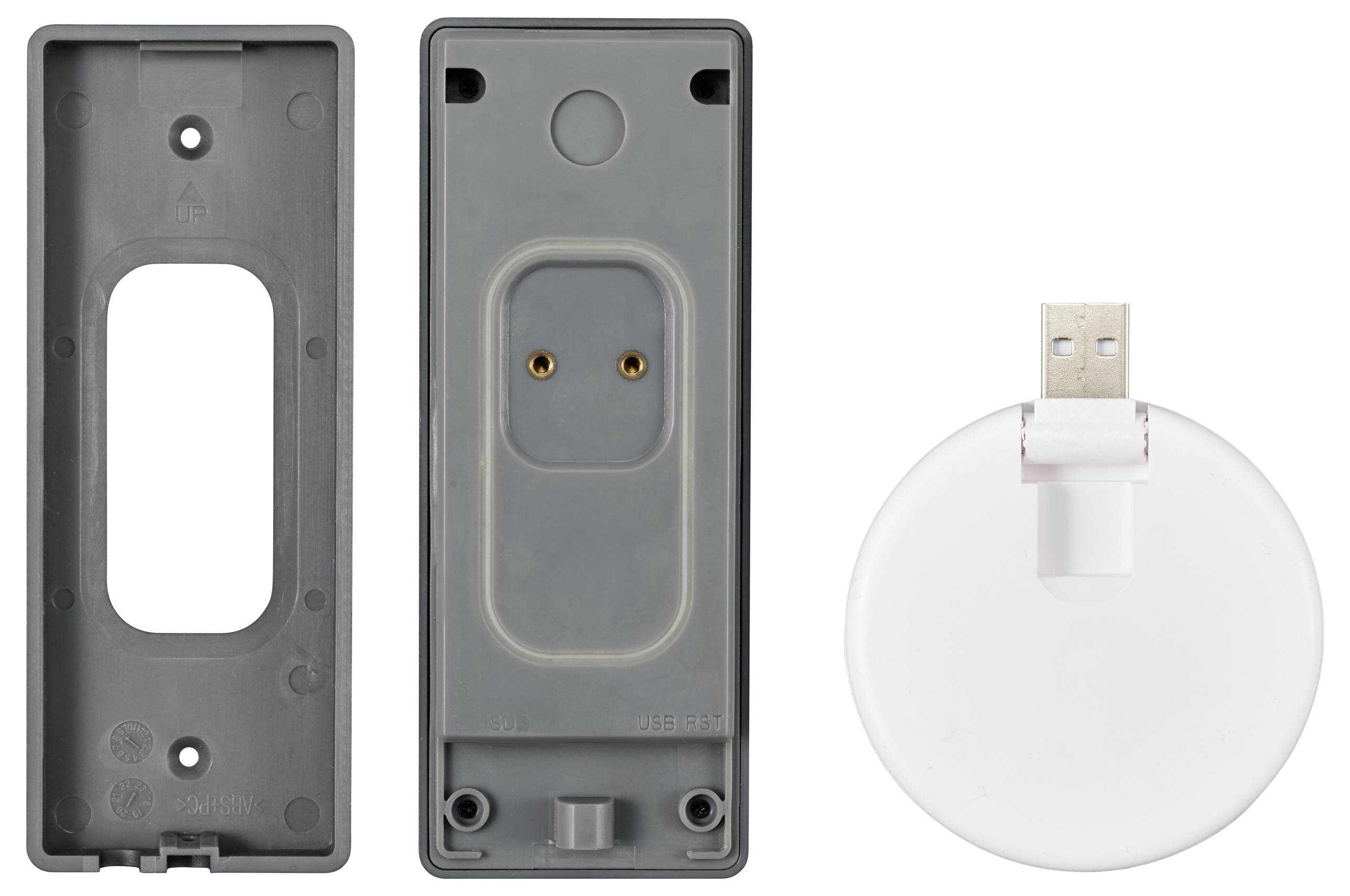 Šedý plastový kryt složený ze dvou částí vedle bílé, kulaté USB nabíjecí stanice. Na zadní straně jsou viditelné kovové kontakty uvnitř.