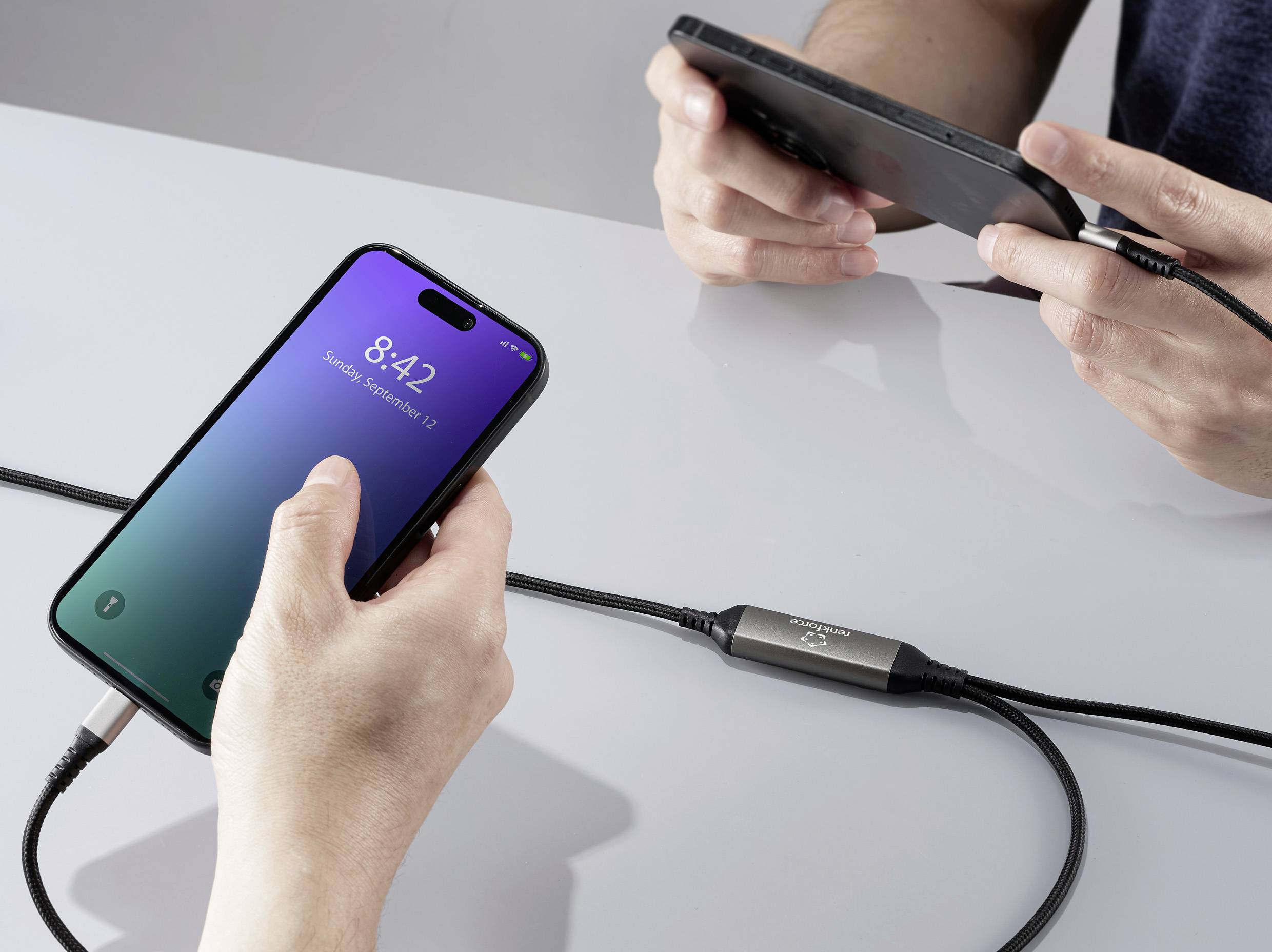 Dvě osoby používají vzájemně propojená digitální zařízení. Vlevo ukazuje obrazovka smartphonu čas 8:42.