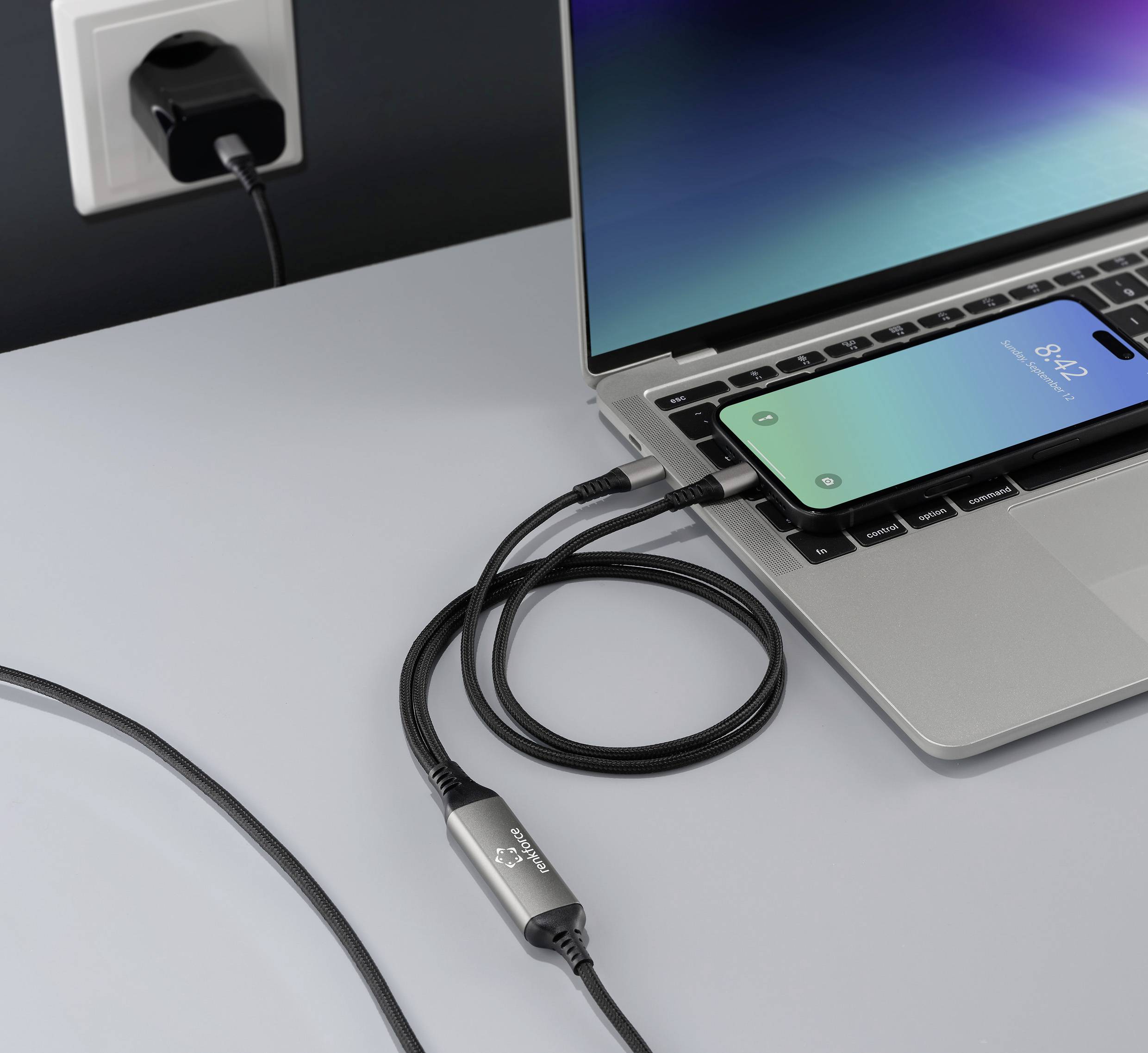 Mobilní telefon je připojen přes USB kabel k laptoptu, na stole se nachází elektrická zásuvka.