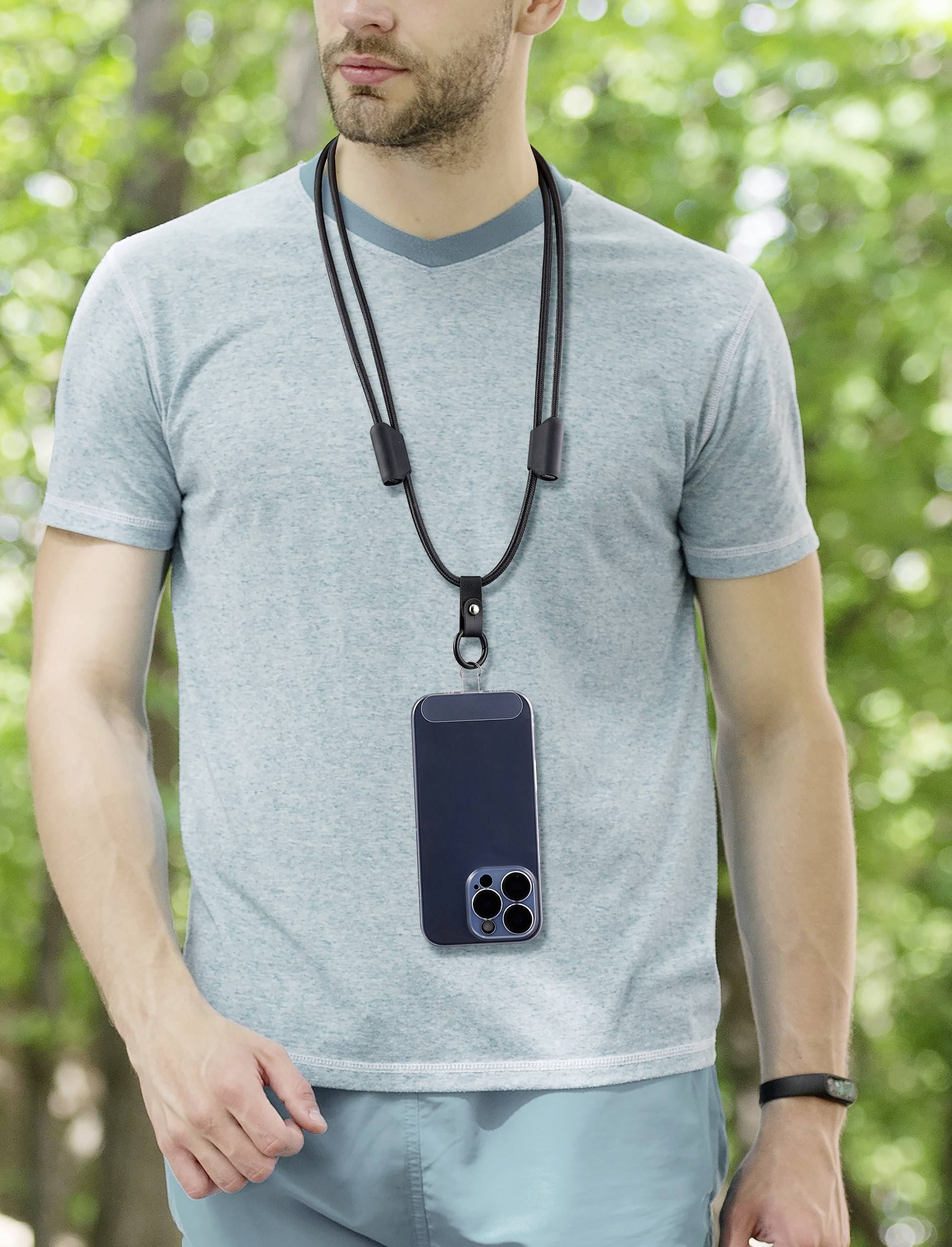 Muž má na sobě světle modré tričko a pouzdro na mobil zavěšené kolem krku v zeleném, lesnatém parku.